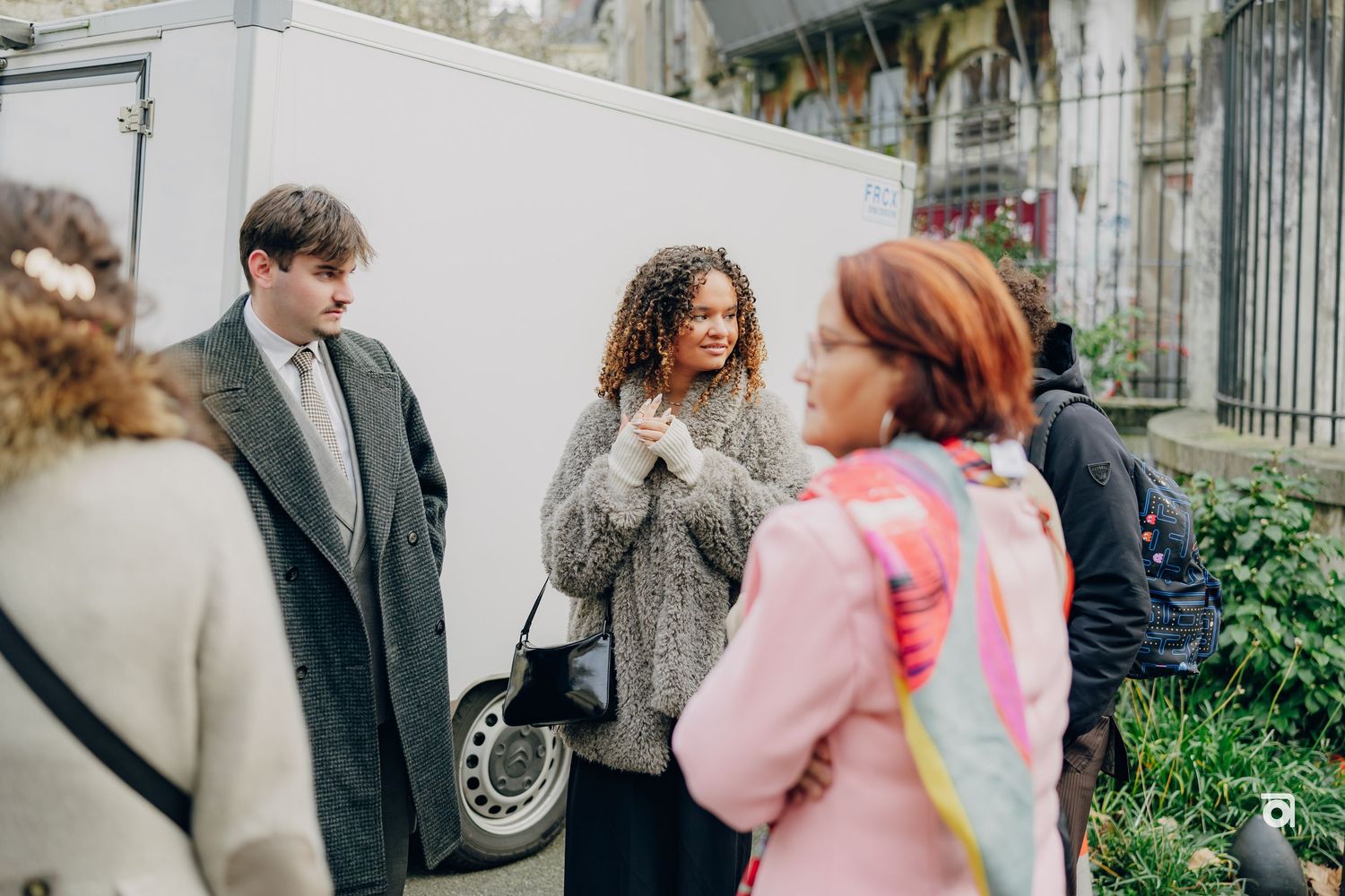 A group of people gathered outside on a winter day, with one wearing a gray coat and another in pink.