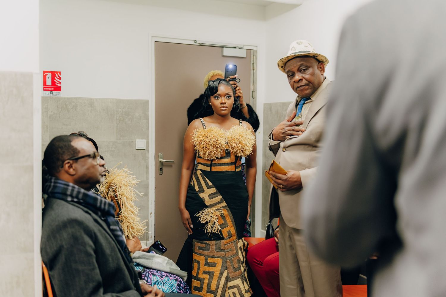 People gathered in a hallway with one person wearing a golden and black patterned dress.