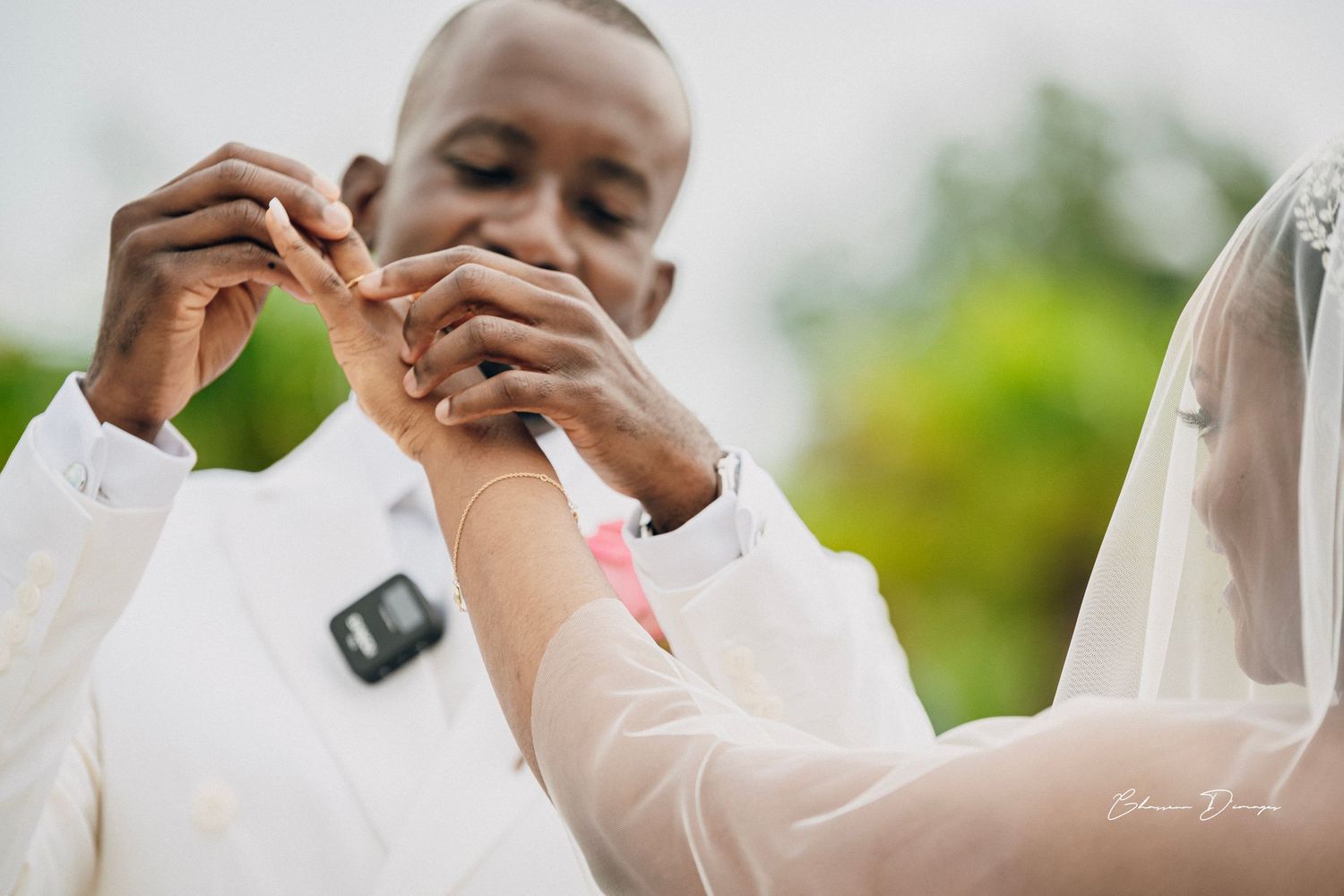 Close-up of joined hands during an outdoor wedding ceremony with a naturalistic green background.