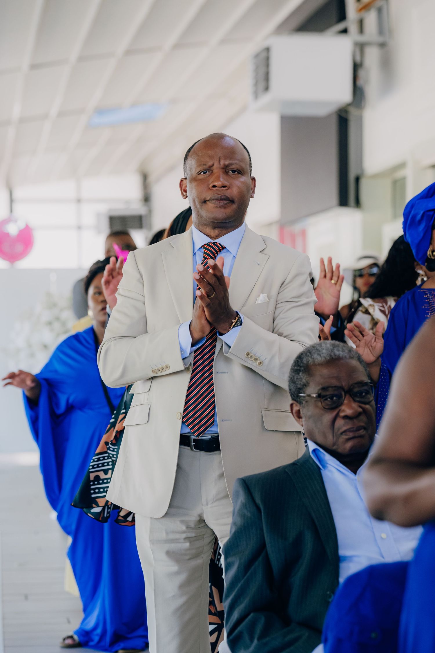 Wedding guests in light suits and blue attire dance and celebrate at a reception.