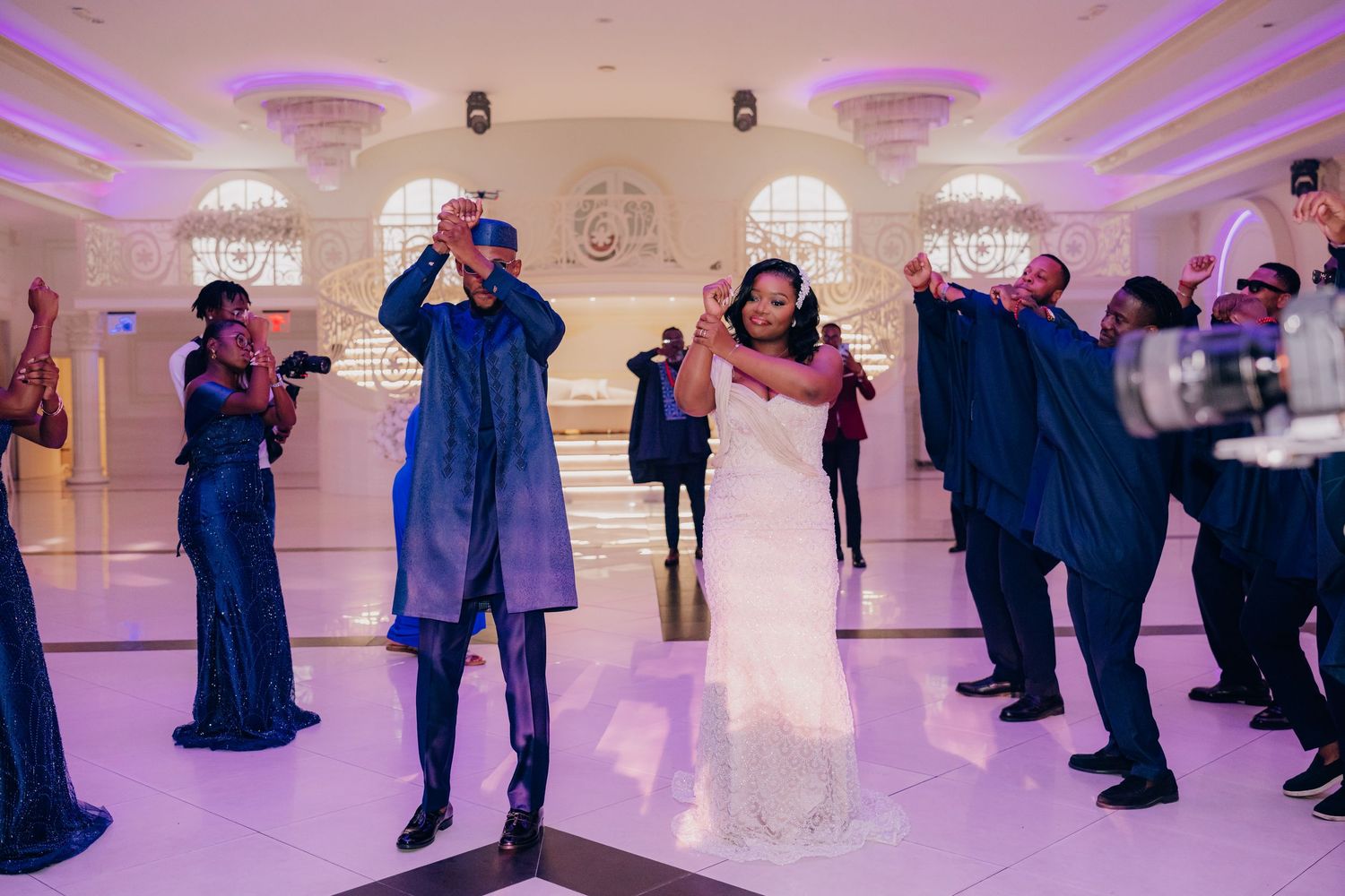 Wedding guests dance and celebrate on the illuminated dance floor with purple ambient lighting.