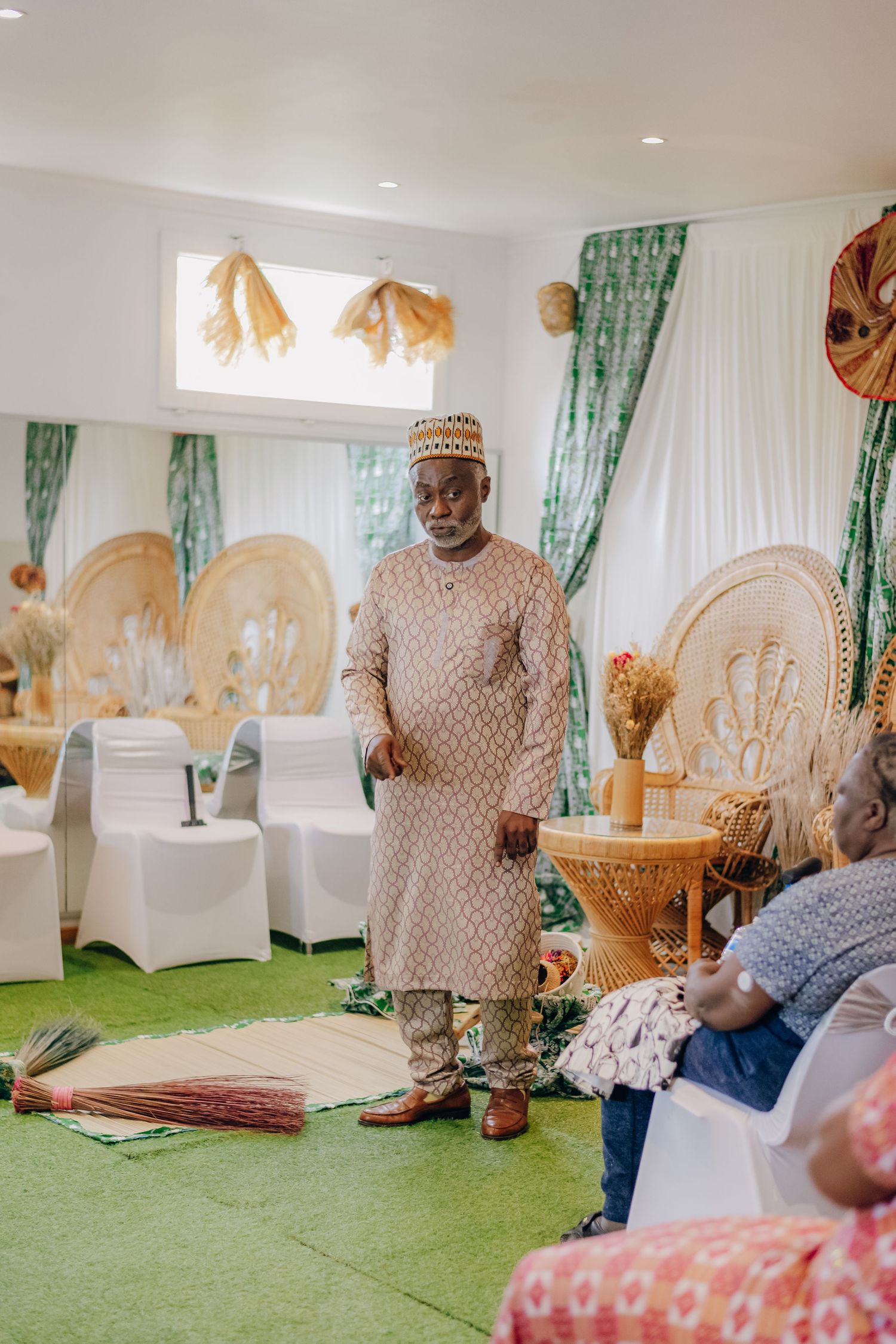 Traditional Nigerian wedding ceremony setup with green curtains, white chairs, and gold decor elements on artificial grass.