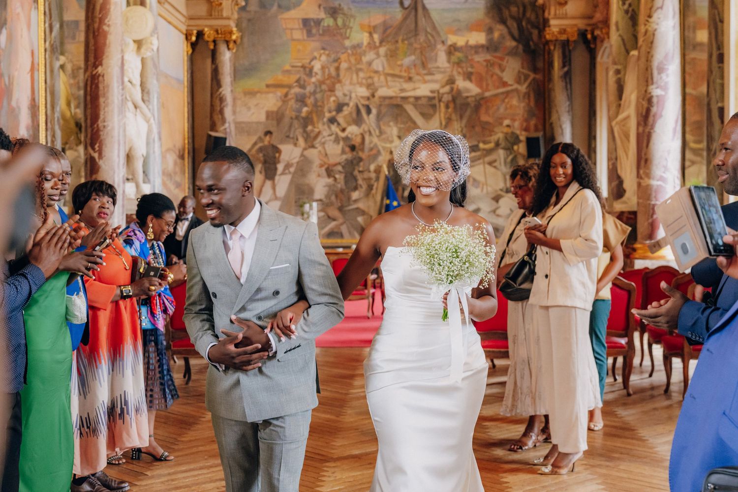 Wedding celebration in a grand baroque hall with guests mingling under ornate frescoed ceilings and gilded details.