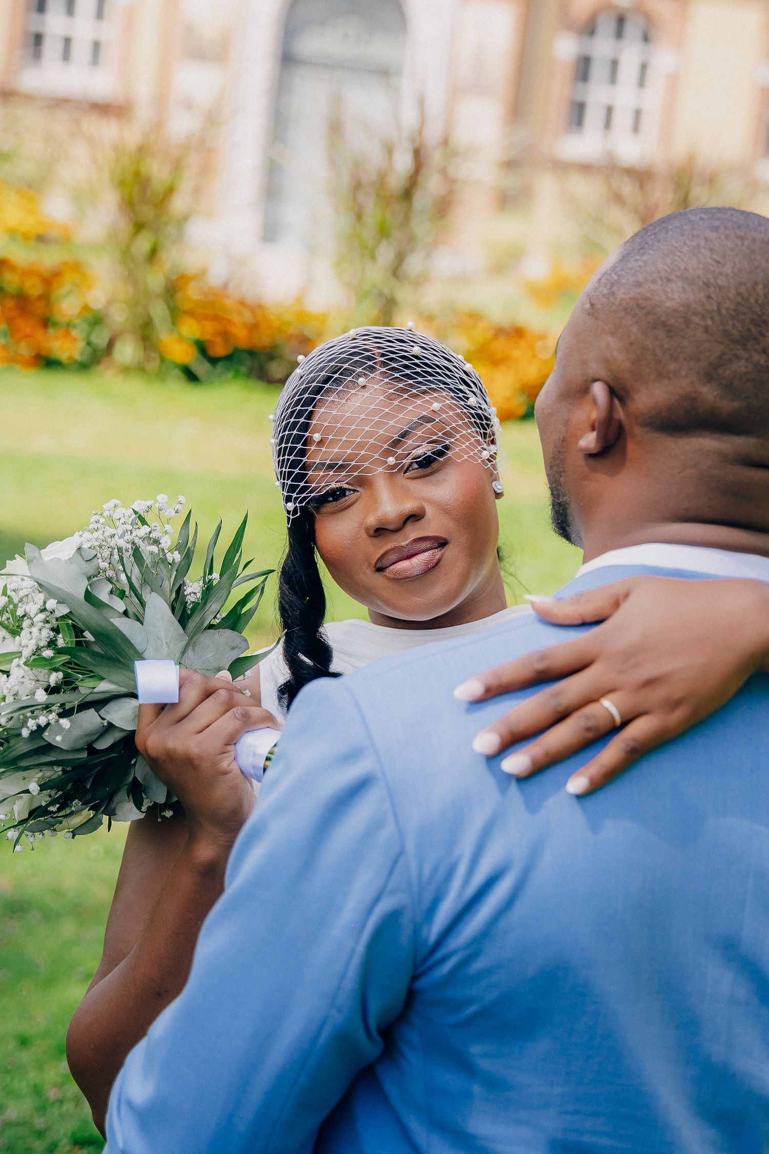 A couple embraces during a wedding photoshoot outdoors with autumn flowers in the background.