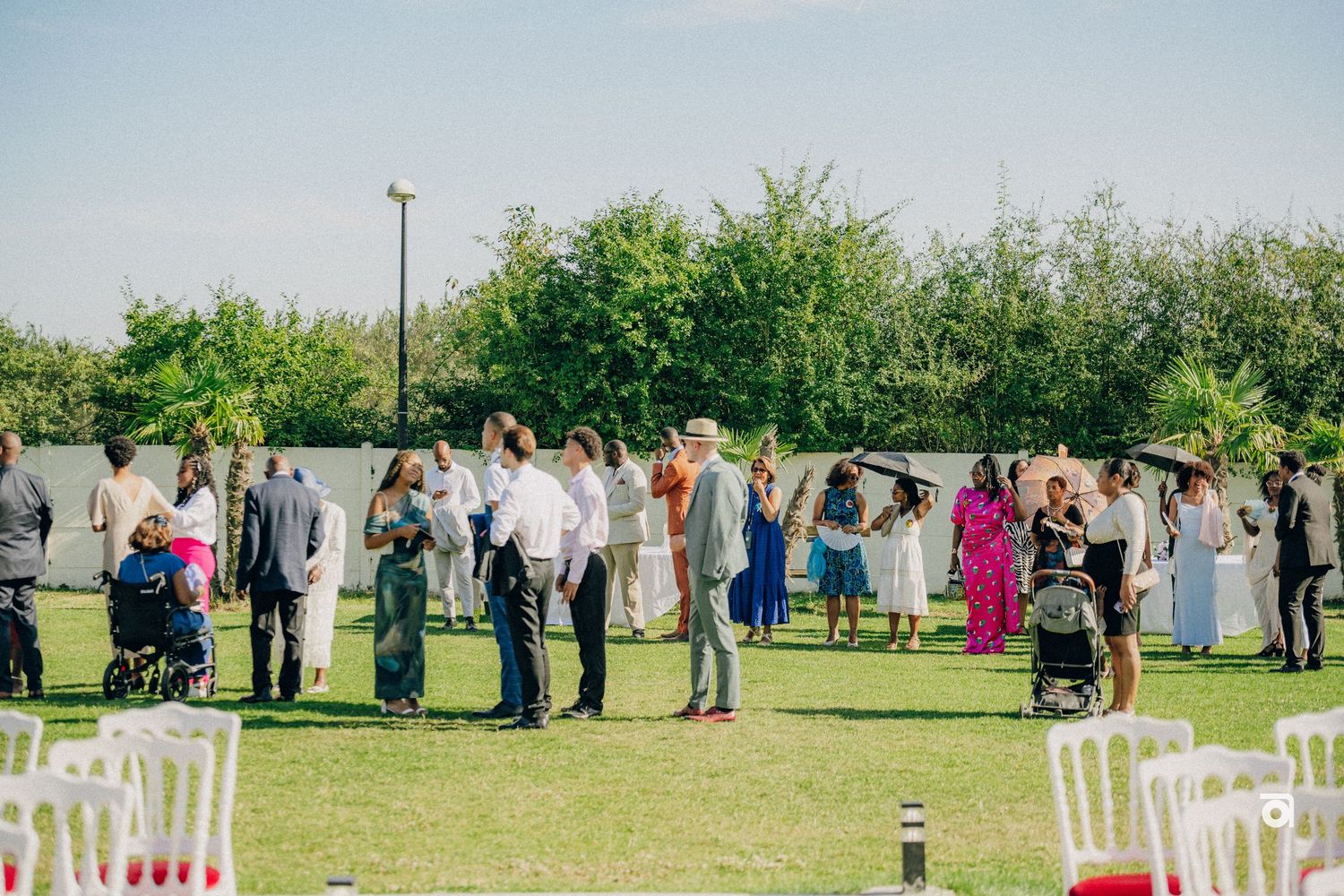 Wedding guests gather on a lush green lawn with white chairs set up for an outdoor ceremony.