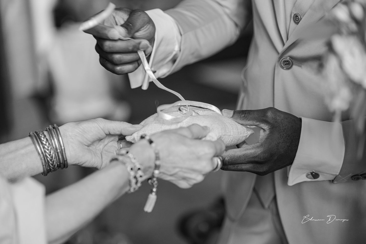 Black and white close-up of hands exchanging rings during wedding ceremony.