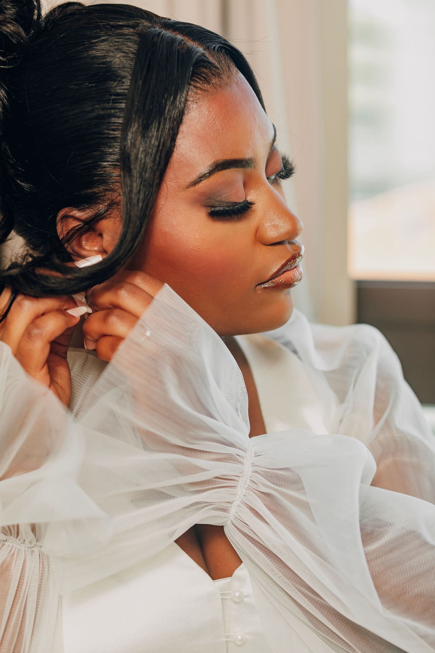 Close-up portrait showing elegant bridal makeup and sheer white fabric details in natural lighting.