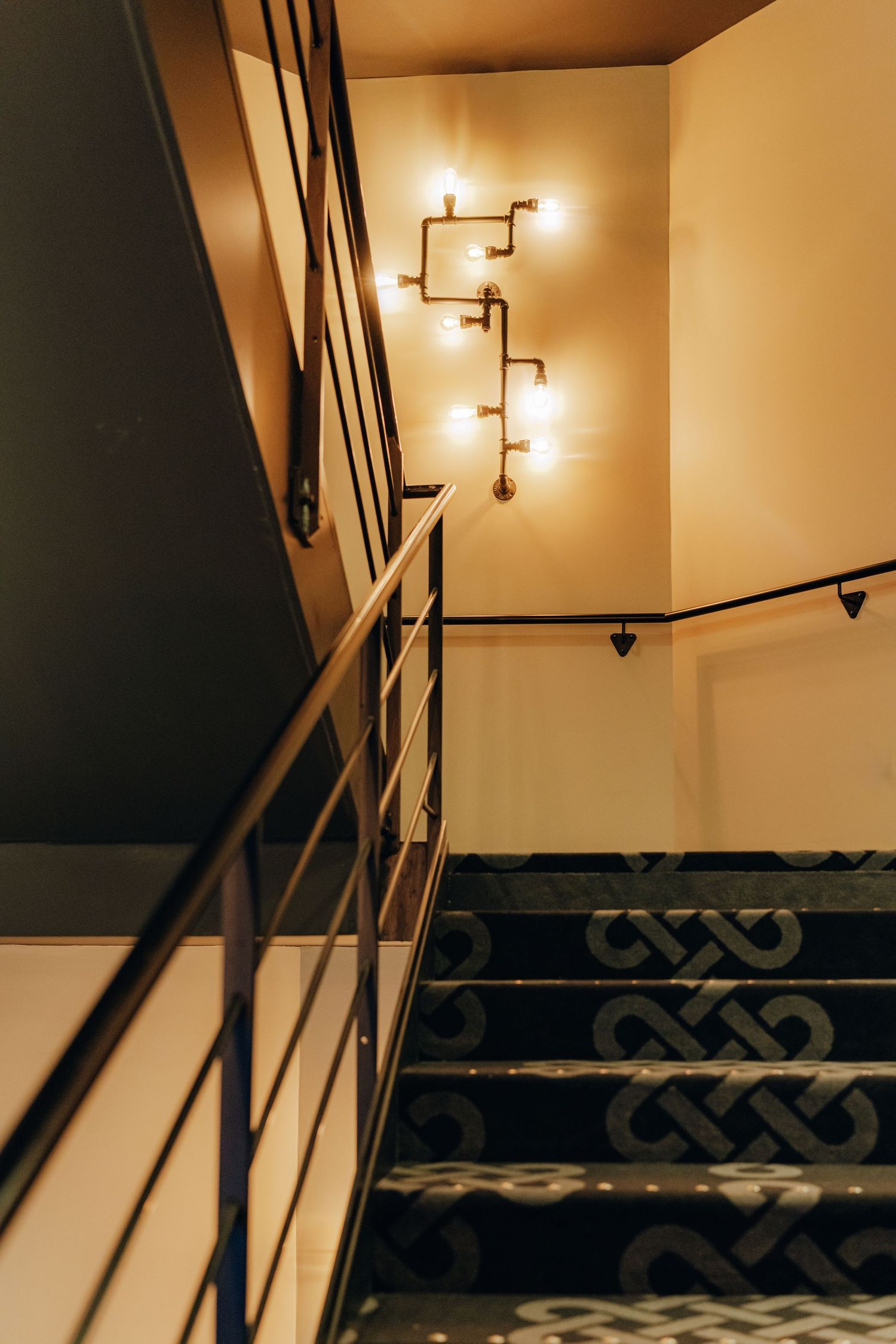 Modern staircase with geometric patterned carpet and warm wall sconce lighting creating an elegant ambiance.