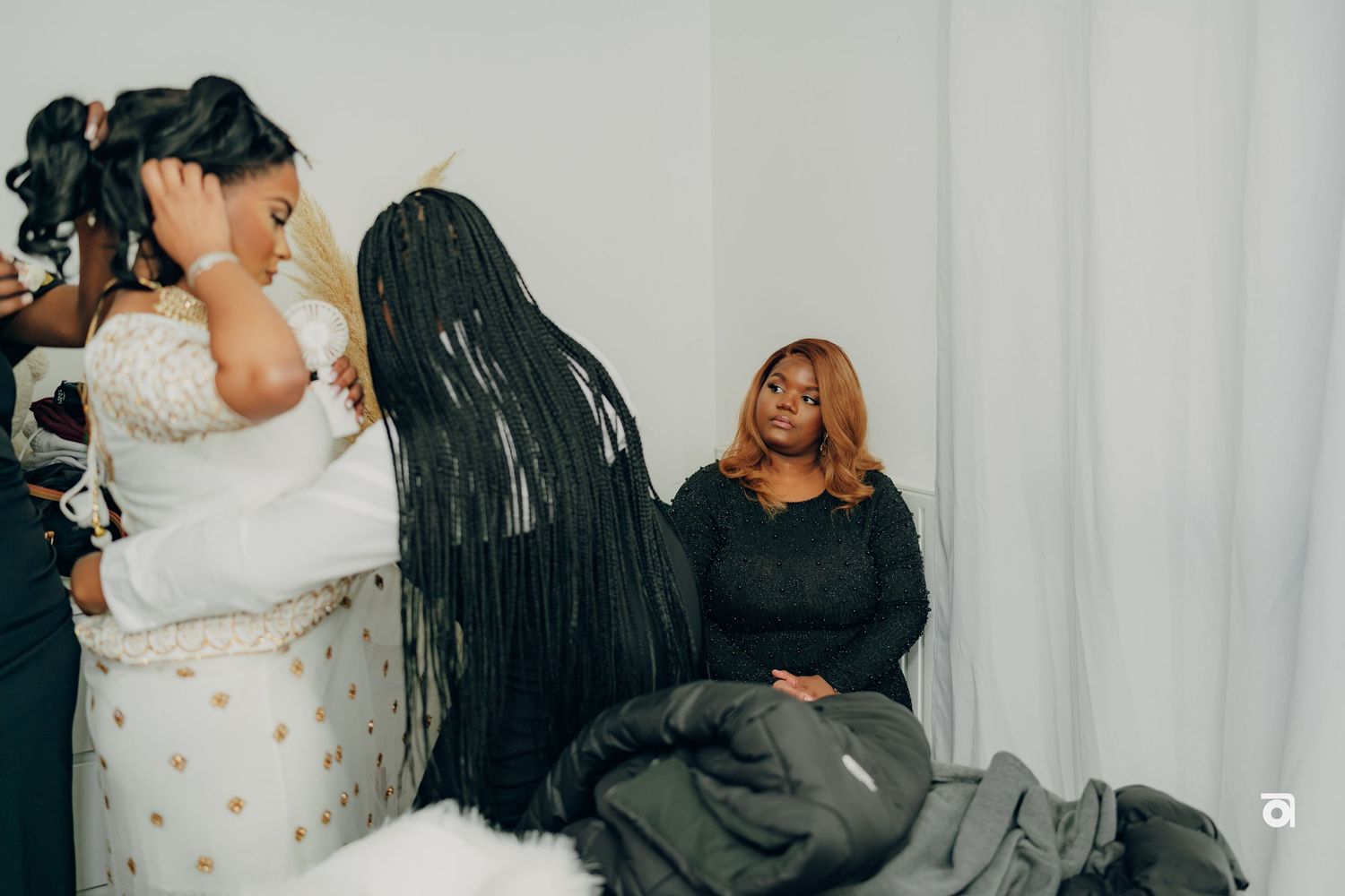 Three people share a candid moment during a wedding dress fitting session in a bridal boutique.