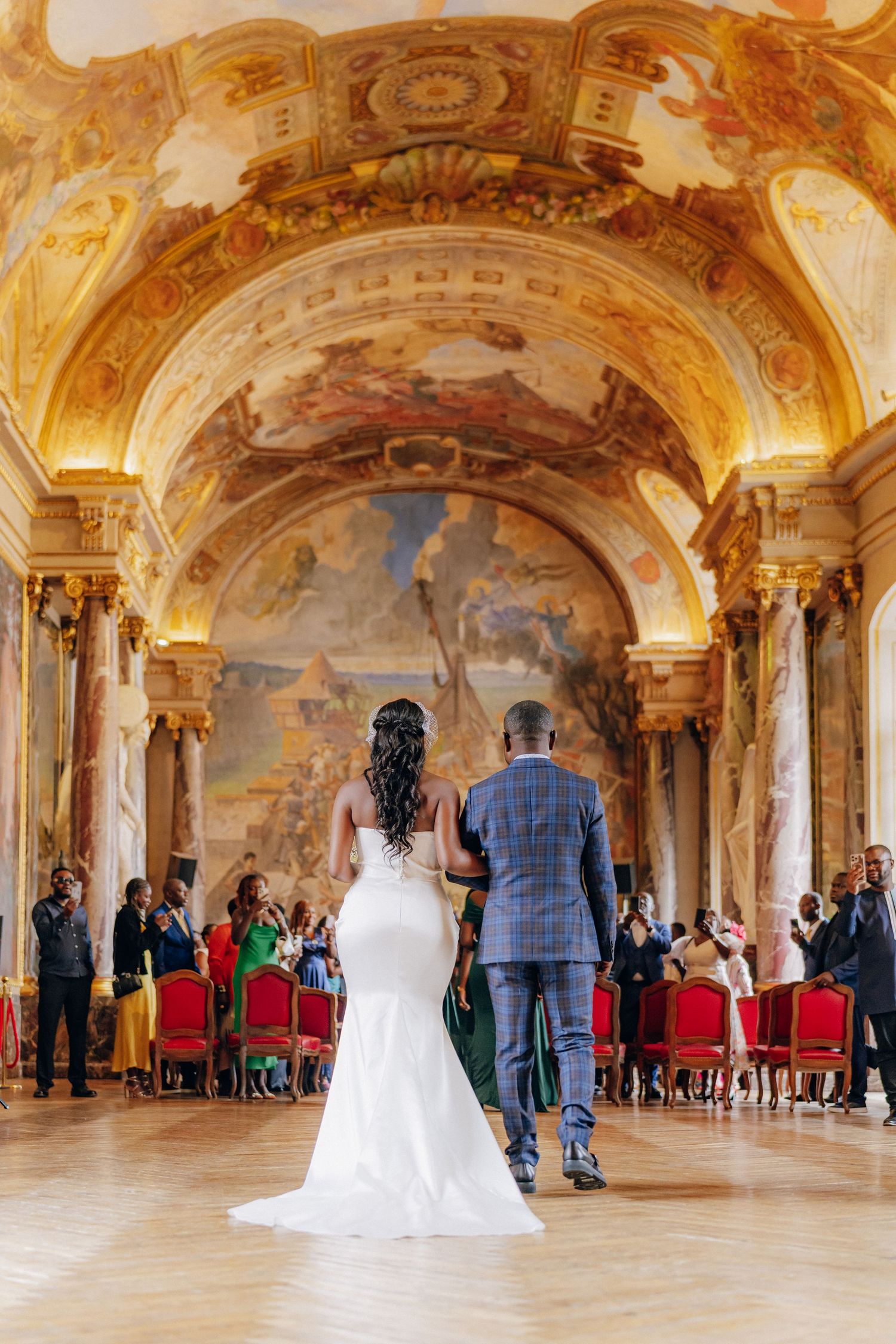 Opulent wedding ceremony in a grand baroque hall with painted ceilings and marble columns.