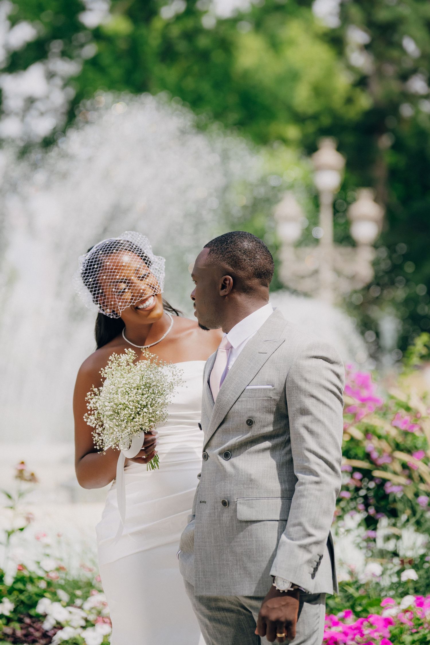 A bride and groom share joyful moments in a garden setting with pink flowers and baby's breath bouquet details.
