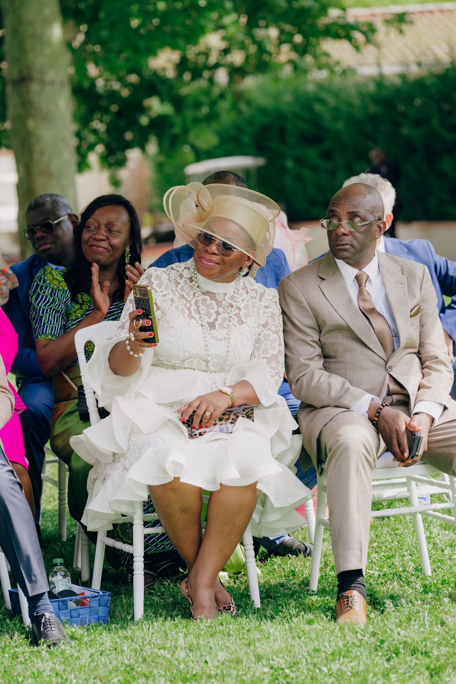 Wedding guests seated in white chairs on a lawn during an outdoor ceremony.
