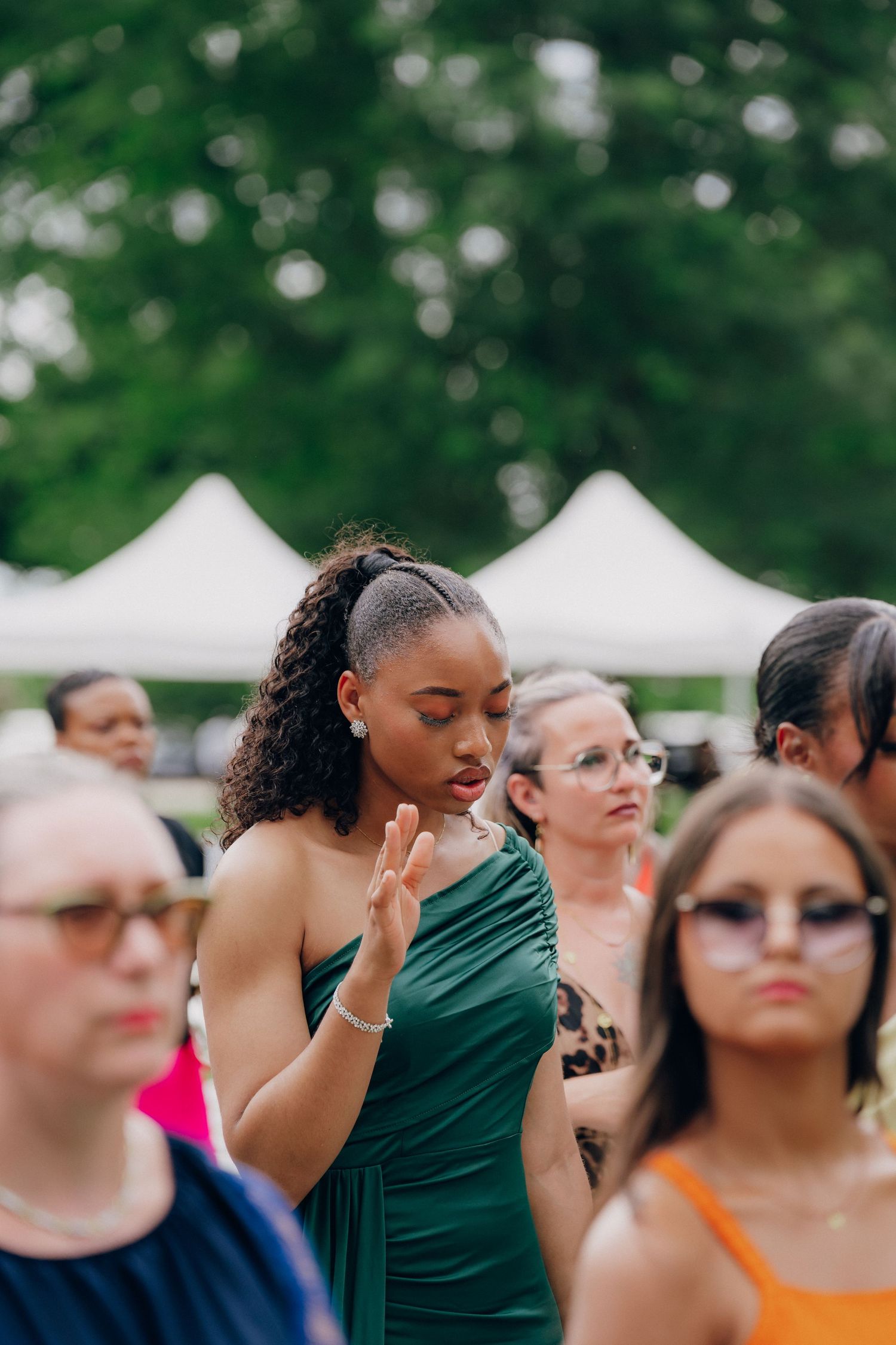 Wedding guests gathered outdoors watching a ceremony with lush green foliage in the background.