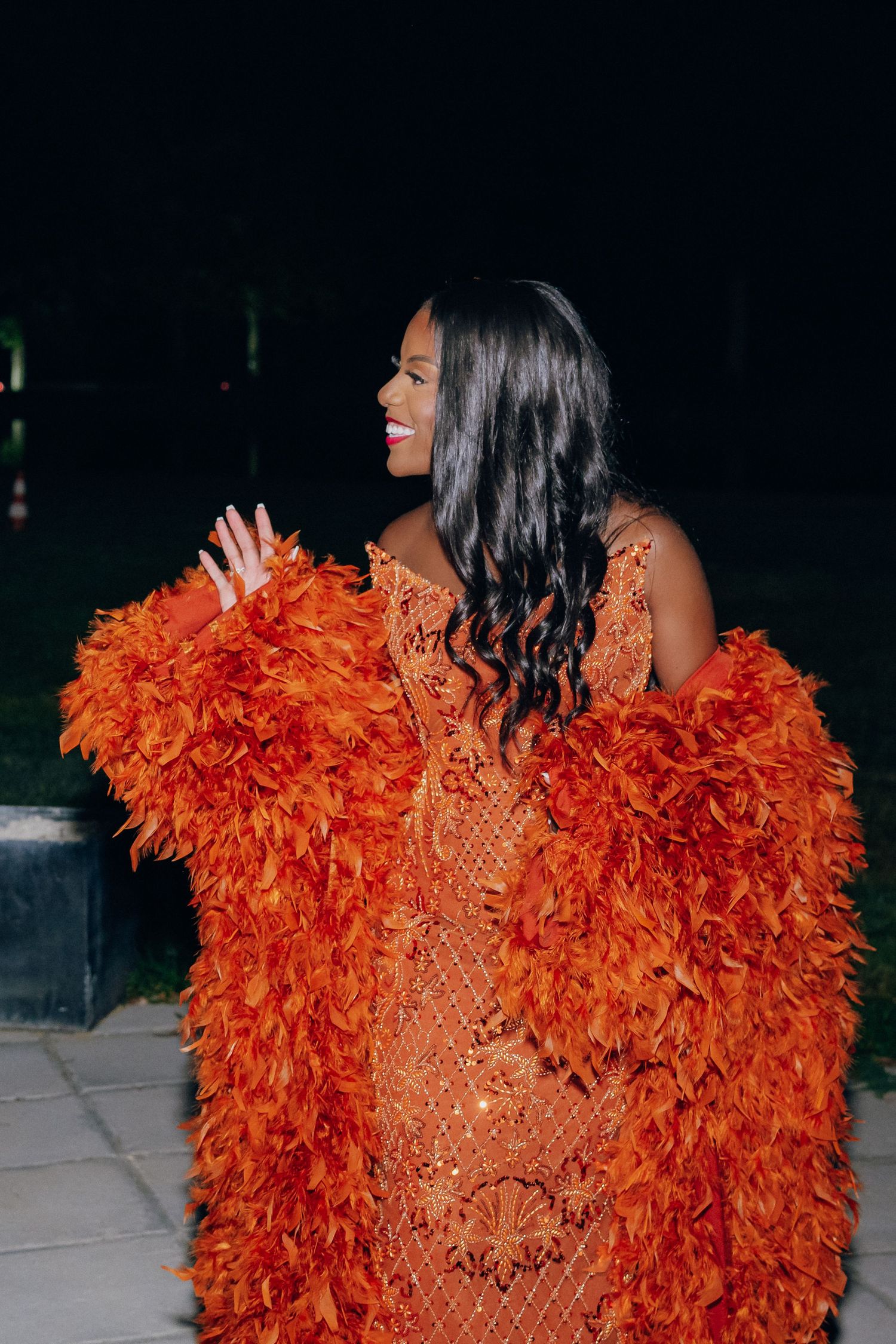 Vibrant orange feathered dress photographed in dramatic lighting at an evening event.