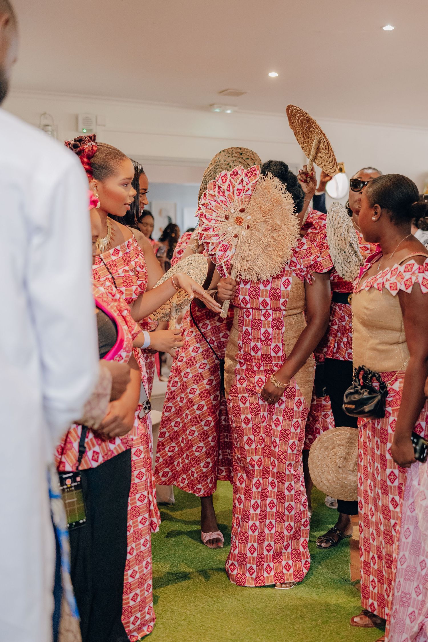 A group wearing matching pink and white patterned outfits gather in a room with green carpet.