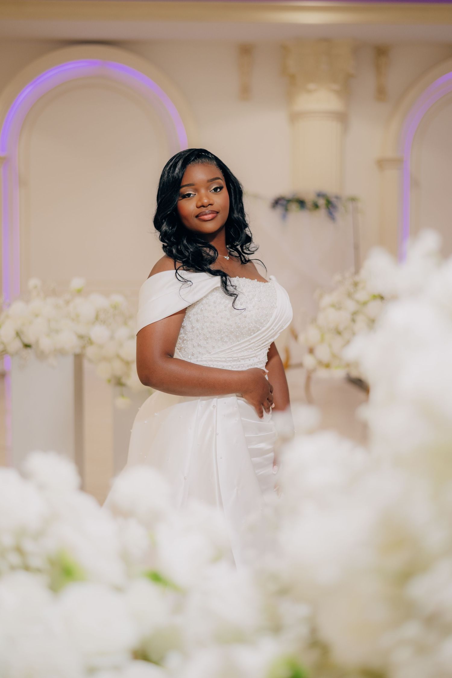 Elegant bridal portraits with soft lighting and white floral decorations in an indoor venue.