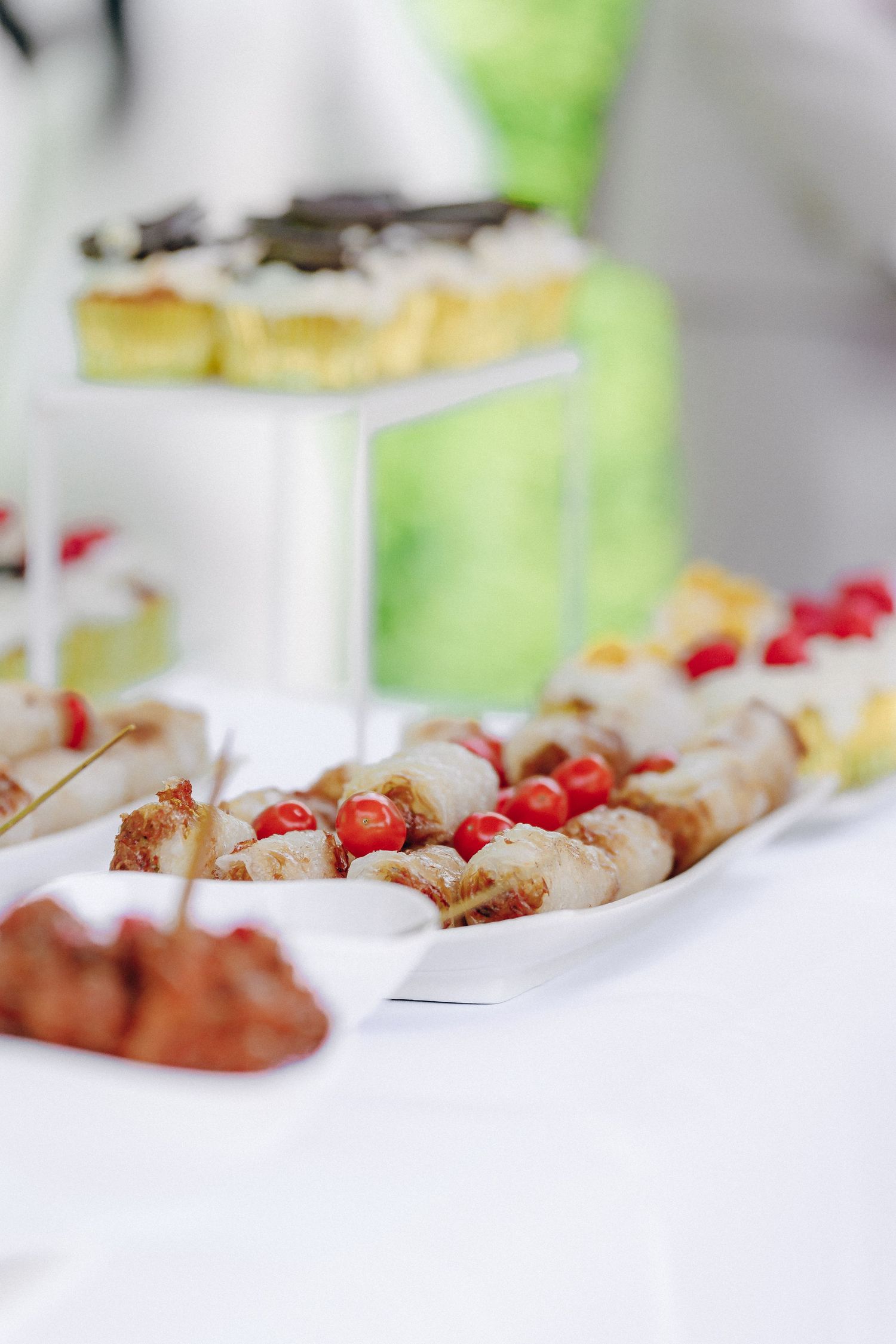 Elegant dessert table display featuring bite-sized pastries and treats garnished with red berries on white serving platters.