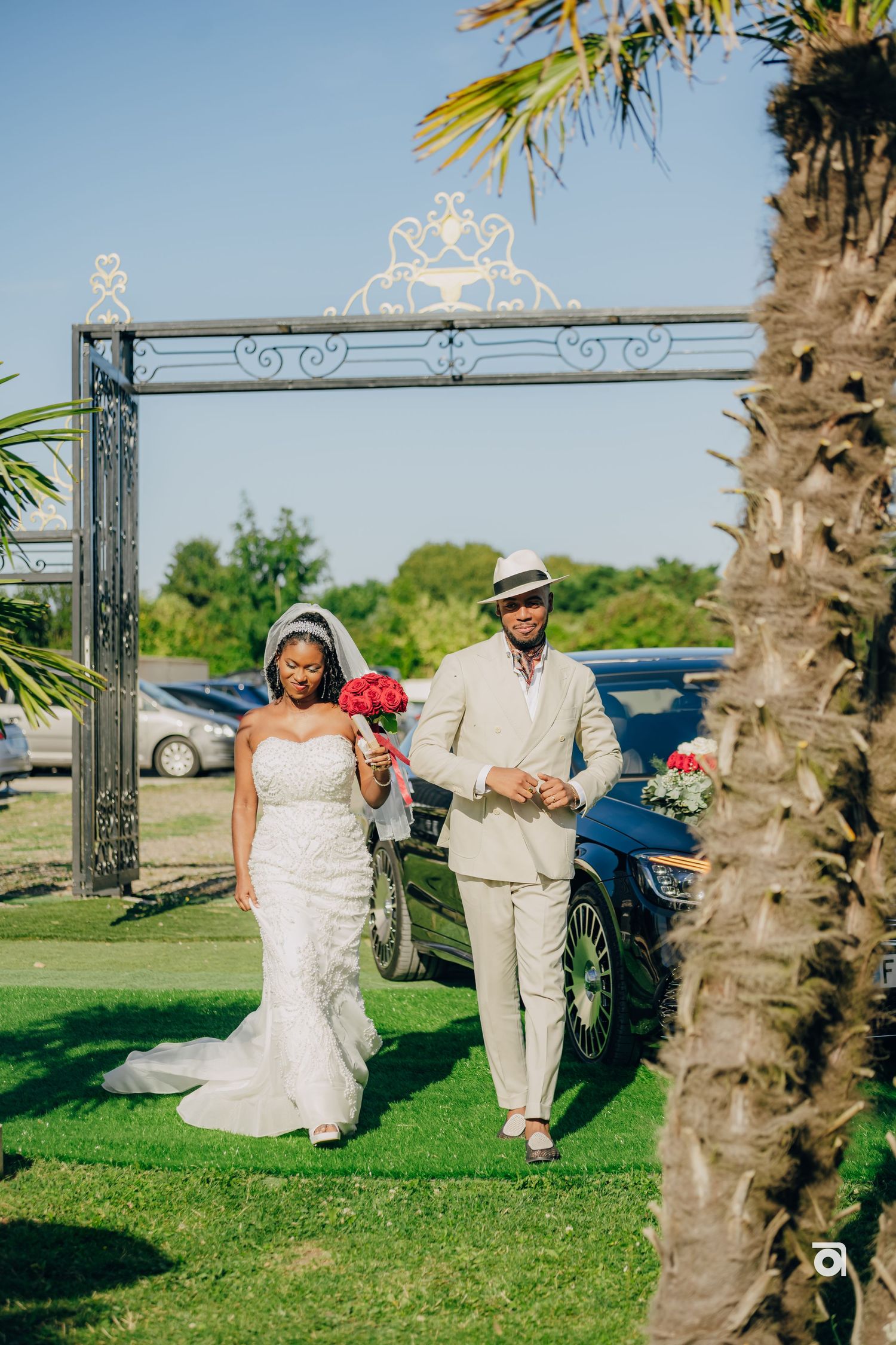 An elegant outdoor wedding ceremony entrance with a decorative metal archway and palm trees against a blue sky.