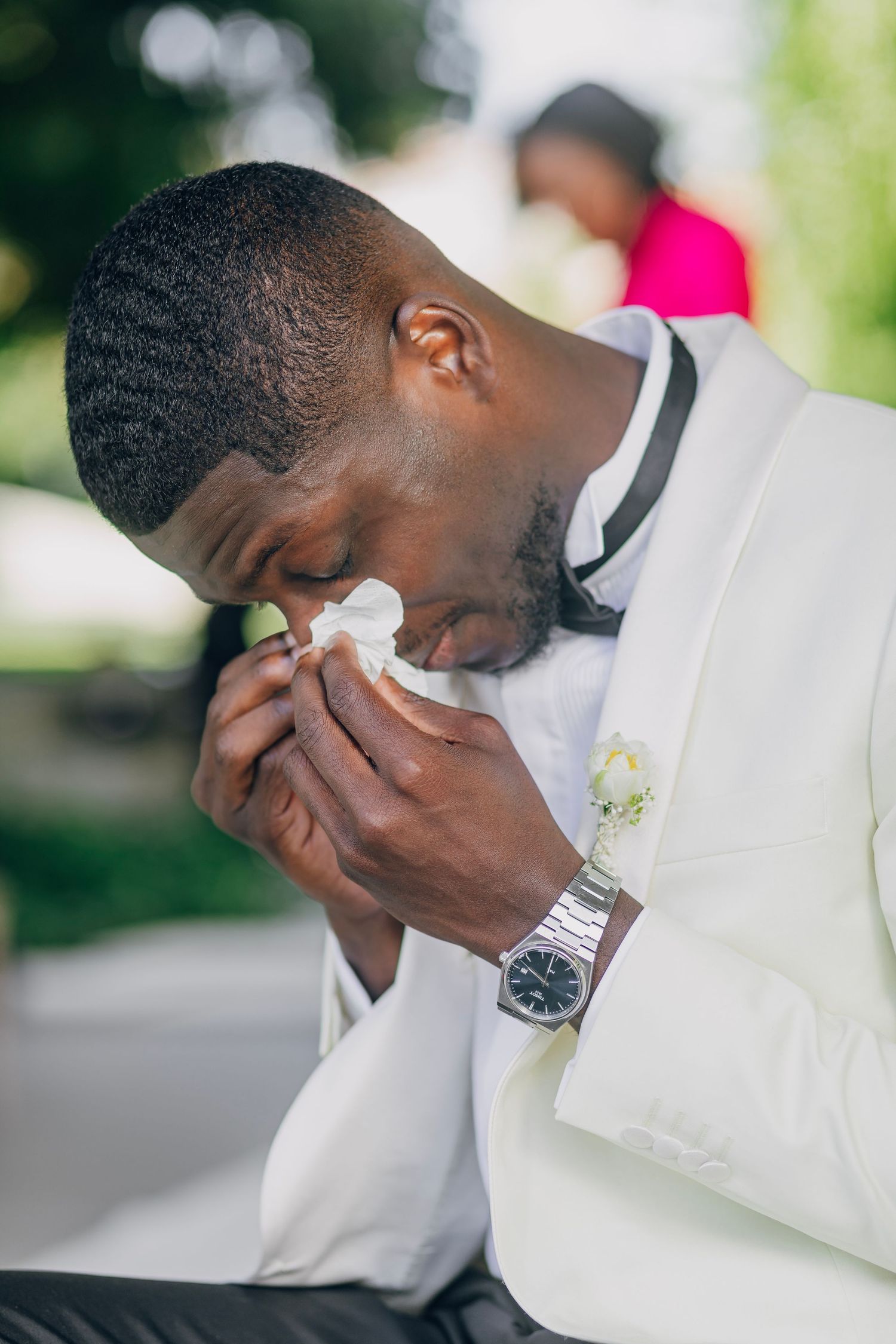 An emotional moment captured as a person in white suit wipes tears during an outdoor ceremony.