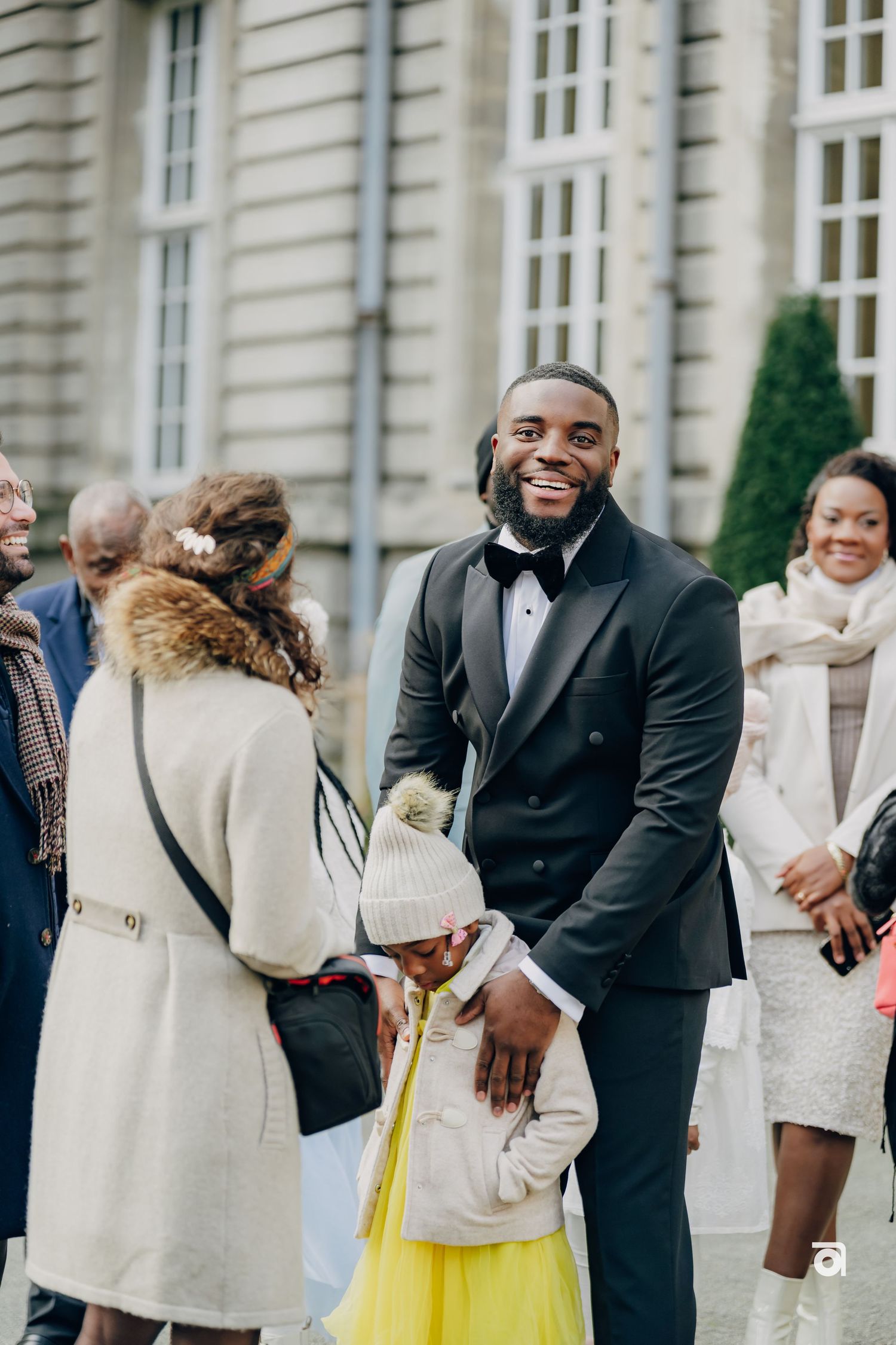 A group of well-dressed guests gather outside an elegant building for a formal occasion.