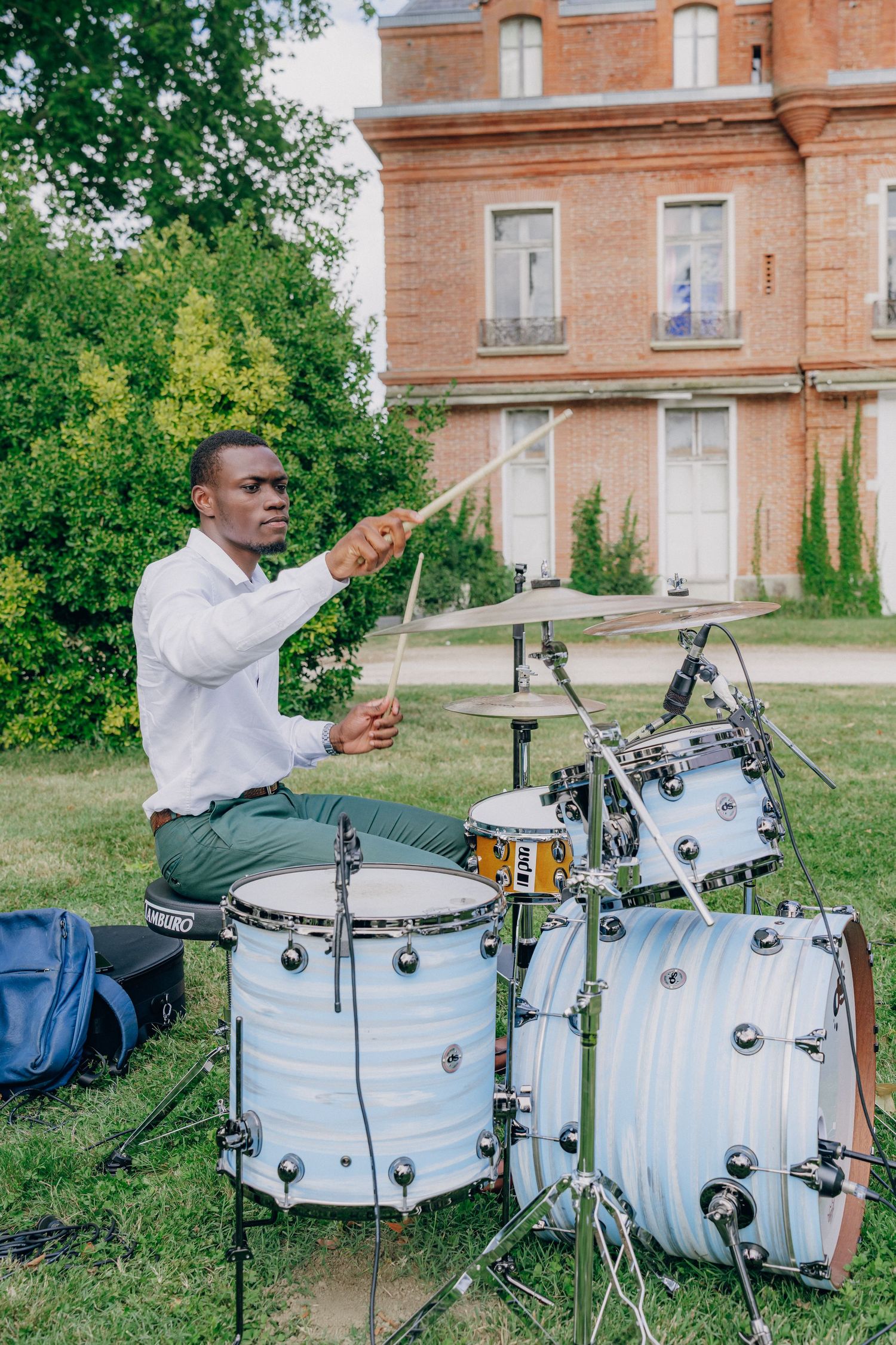 Drummer performs on a white drum kit outside a historic brick building.