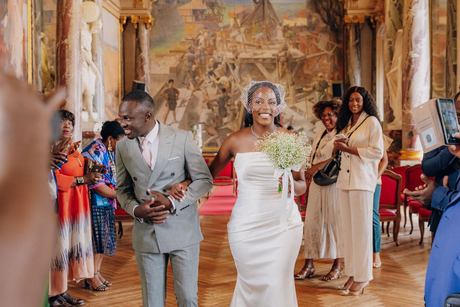 Wedding guests mingling in an ornate palace corridor with historic frescoes and classical architecture.