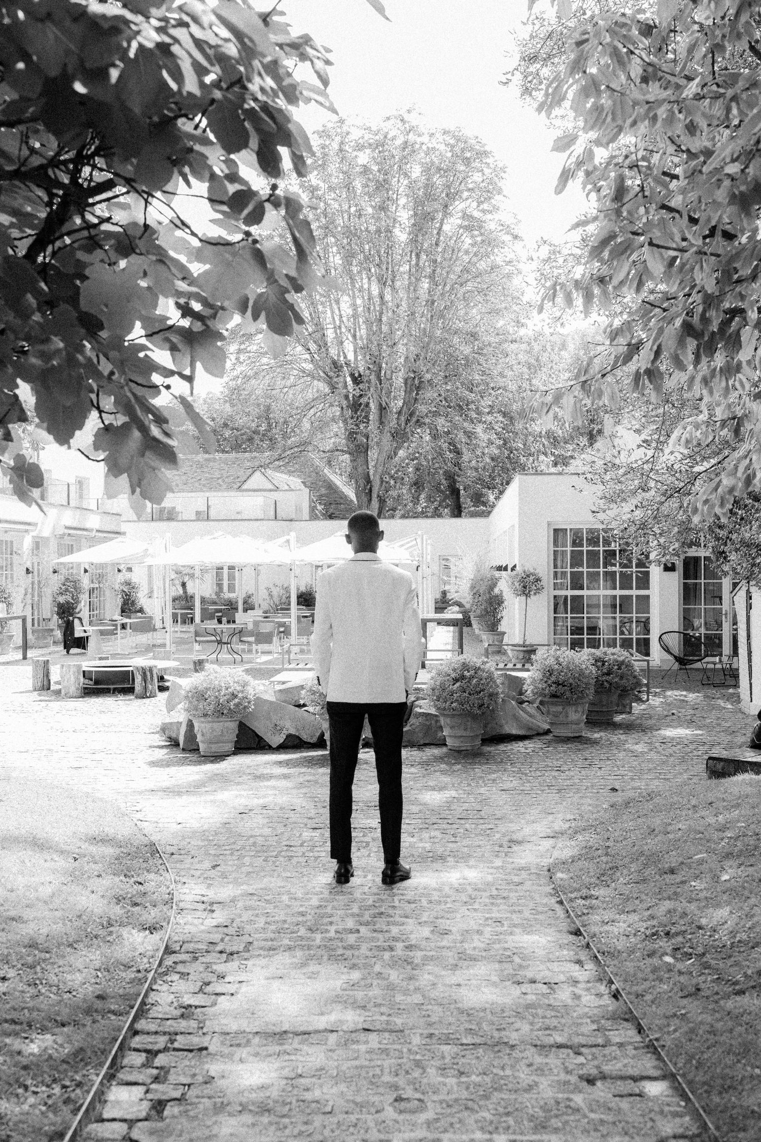 Black and white photo series showing a person walking along a garden path surrounded by trees and landscaping.