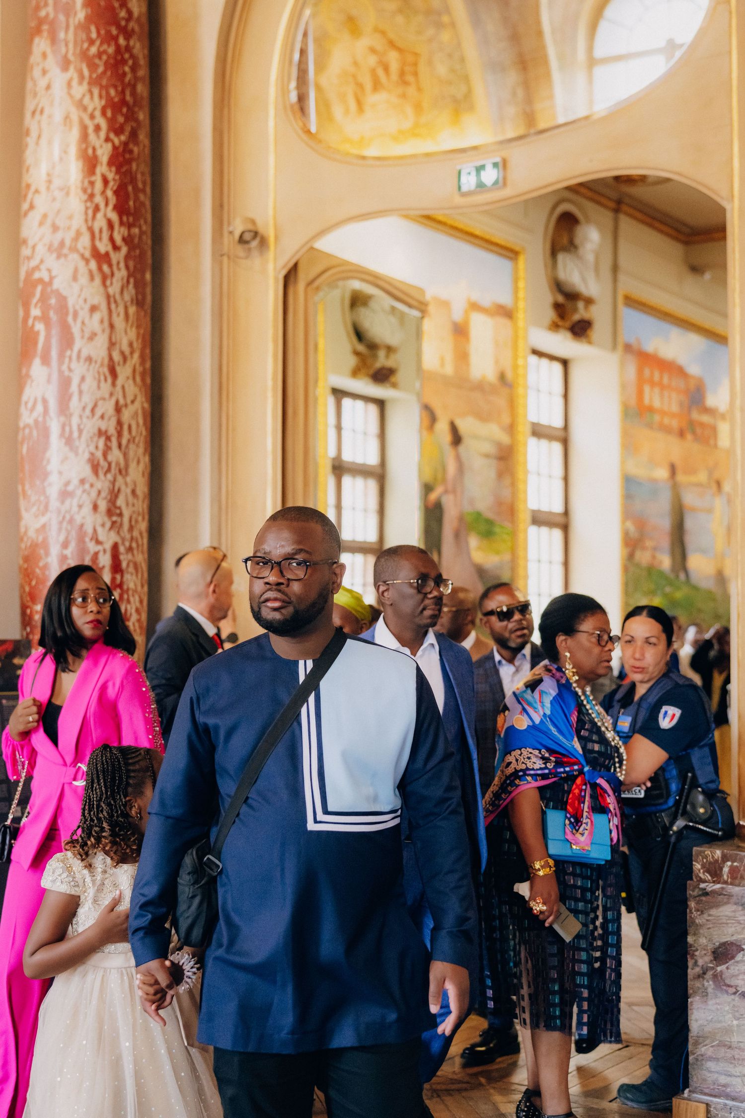 A group of guests gather in an elegant hallway with marble columns and ornate decor during a formal event.