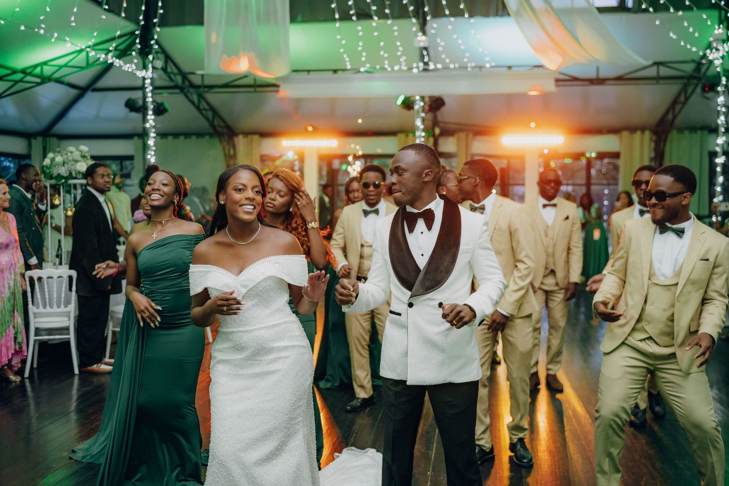 Wedding party dancing together in formal attire with emerald green and beige color scheme.