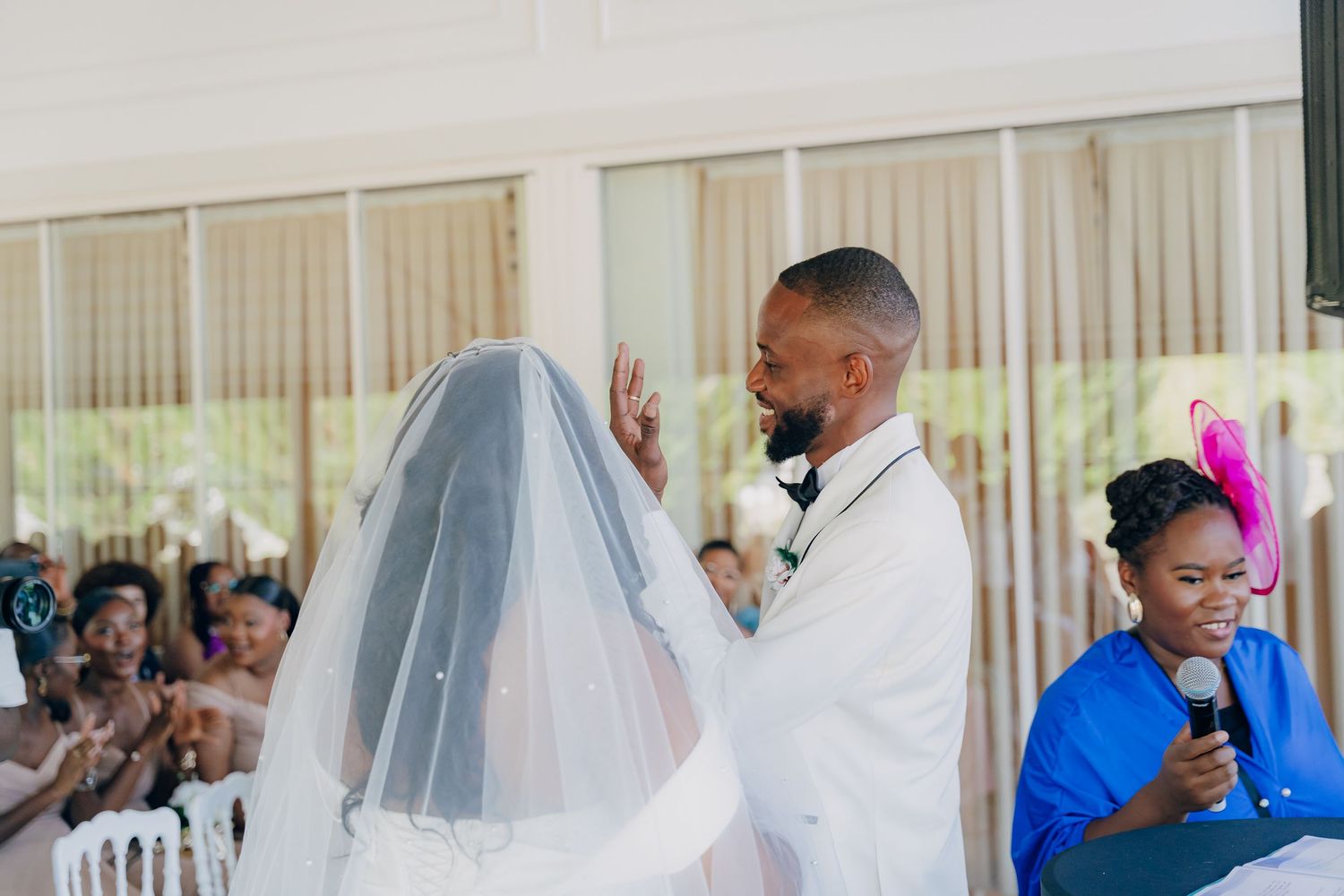 Groom lifts bride's veil during wedding ceremony while guests look on.