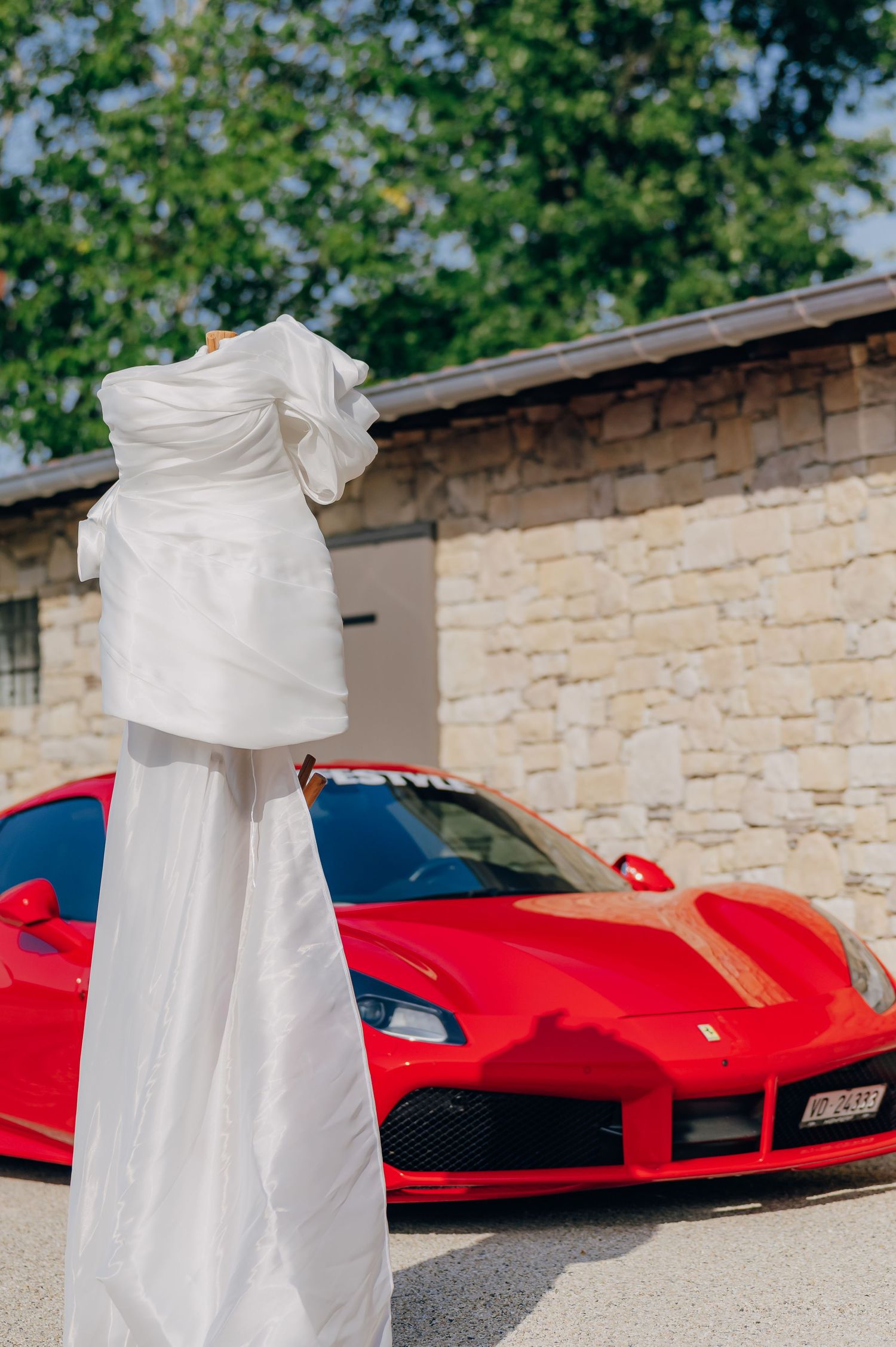 A red Ferrari sports car parked against a stone wall backdrop with elegant white wedding dress details visible.