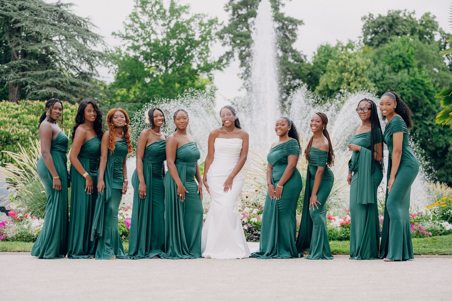 A wedding party in emerald green bridesmaid dresses poses together in an outdoor garden setting.