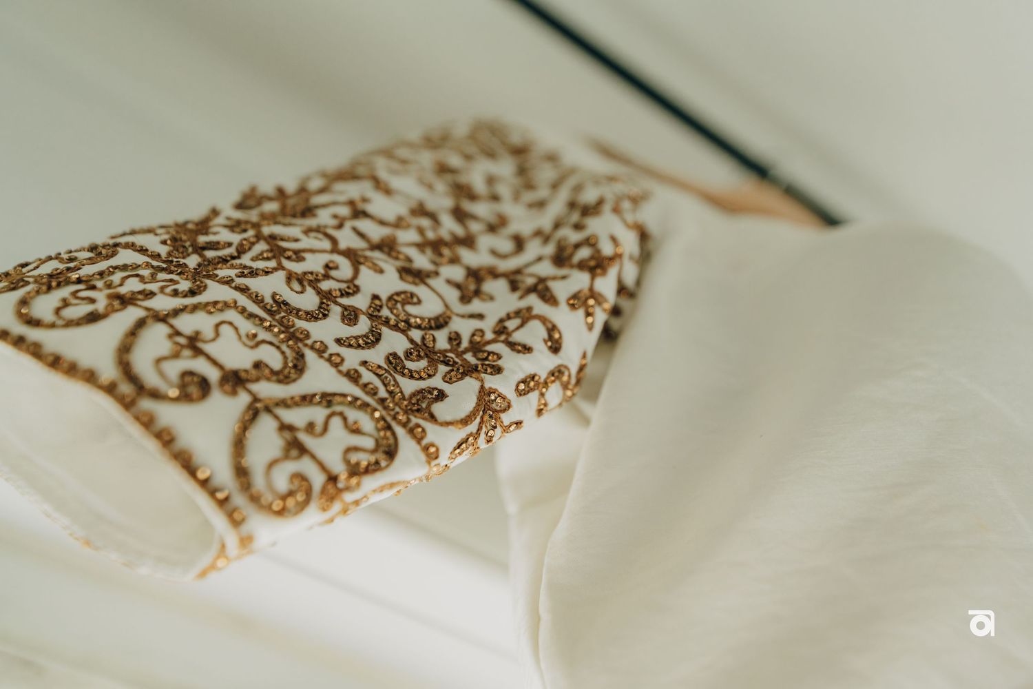 Close-up detail of gold embroidered pattern on white fabric.