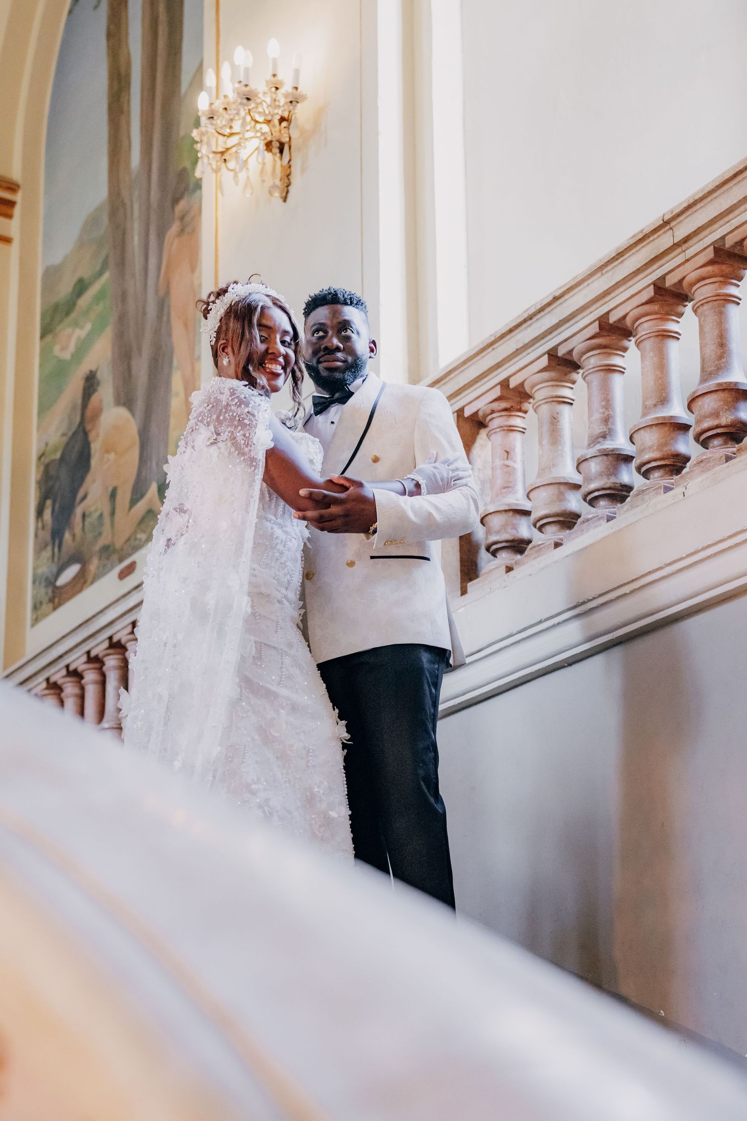 A couple shares a romantic dance in an elegant hallway with ornate chandeliers and artwork adorning the walls.