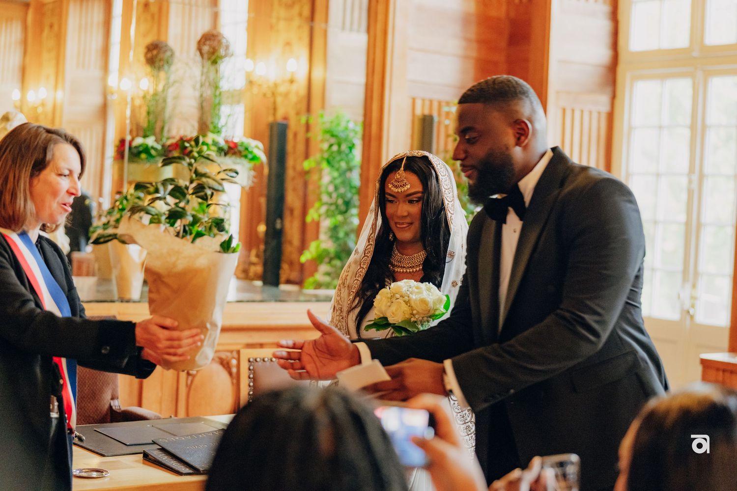 Wedding gathering in a sunlit room with potted plants and elegant decor.