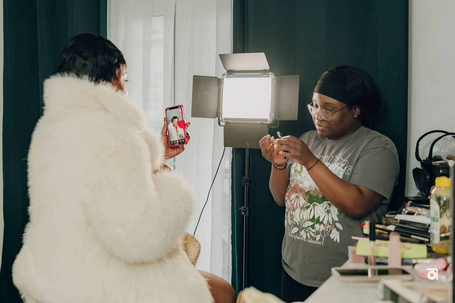 Two people in casual clothing stand in a room while one uses a phone and another appears to be talking.