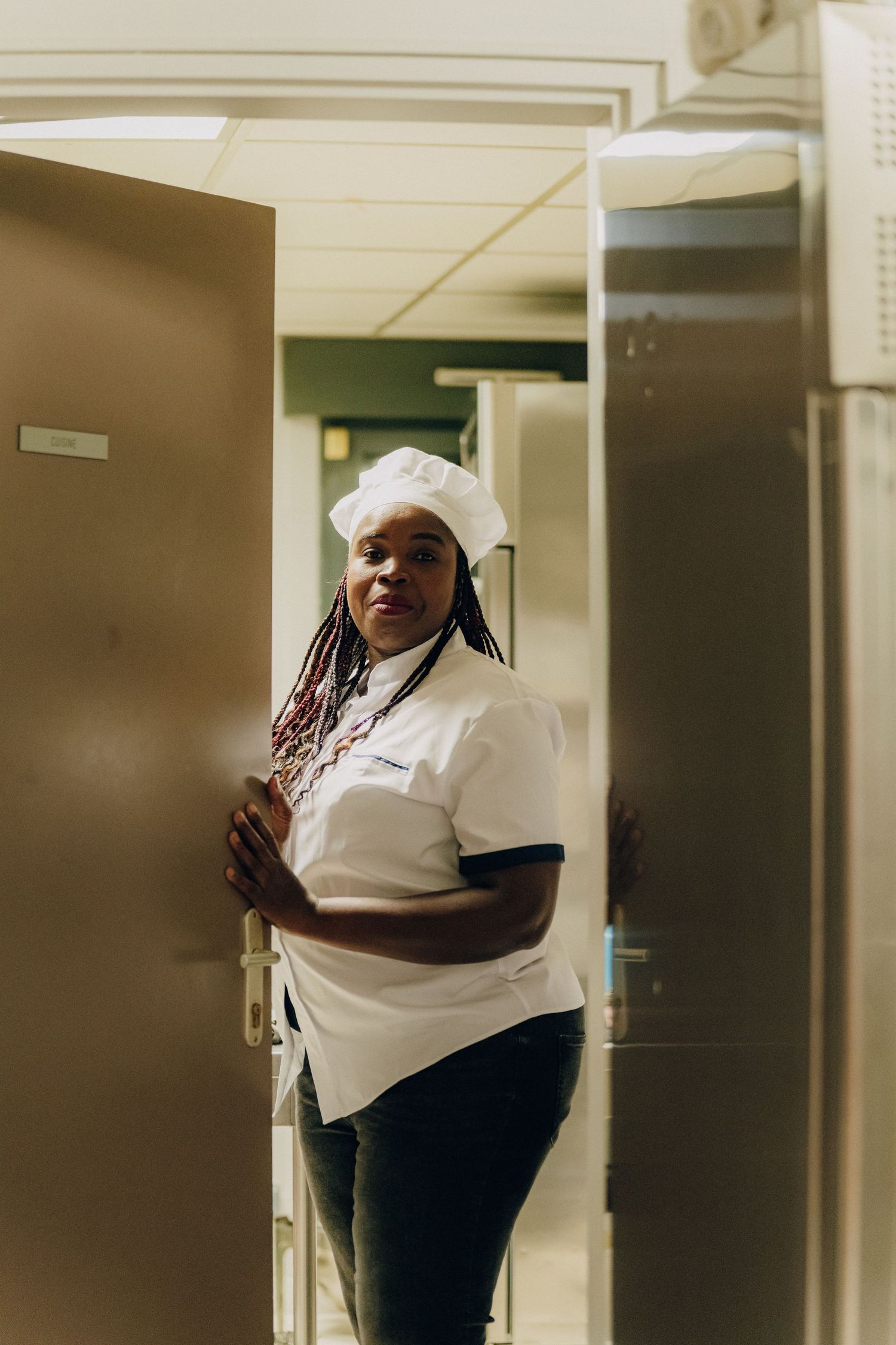 A food service worker in white uniform standing in a hallway.