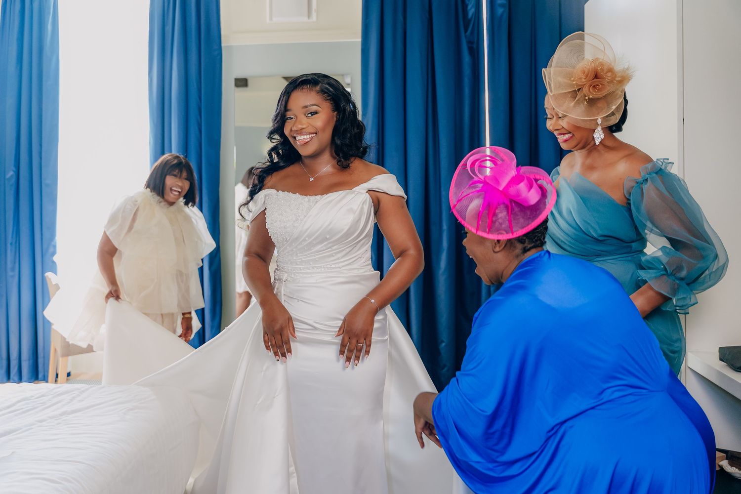 Wedding party members pose together wearing elegant blue and white dresses against blue curtains.