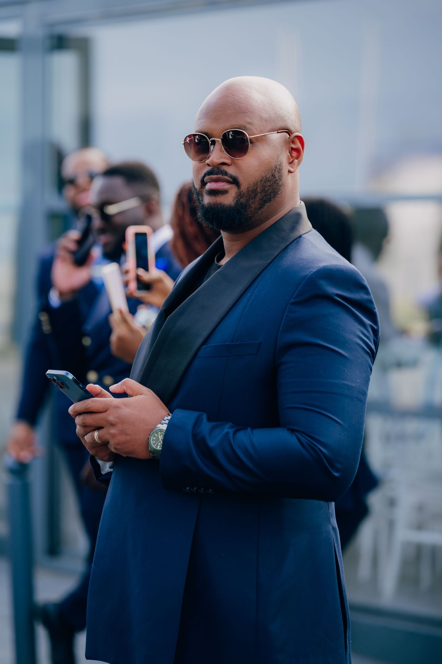 Groomsmen in navy suits taking photos on their phones at an outdoor venue.
