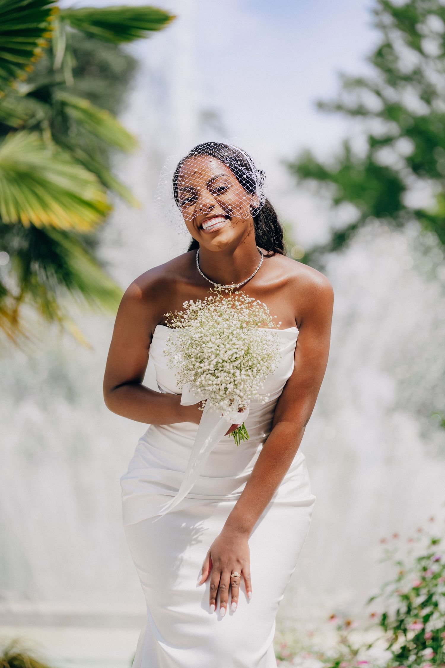 A joyful moment captured in a white strapless gown with baby's breath flowers against a tropical palm background.