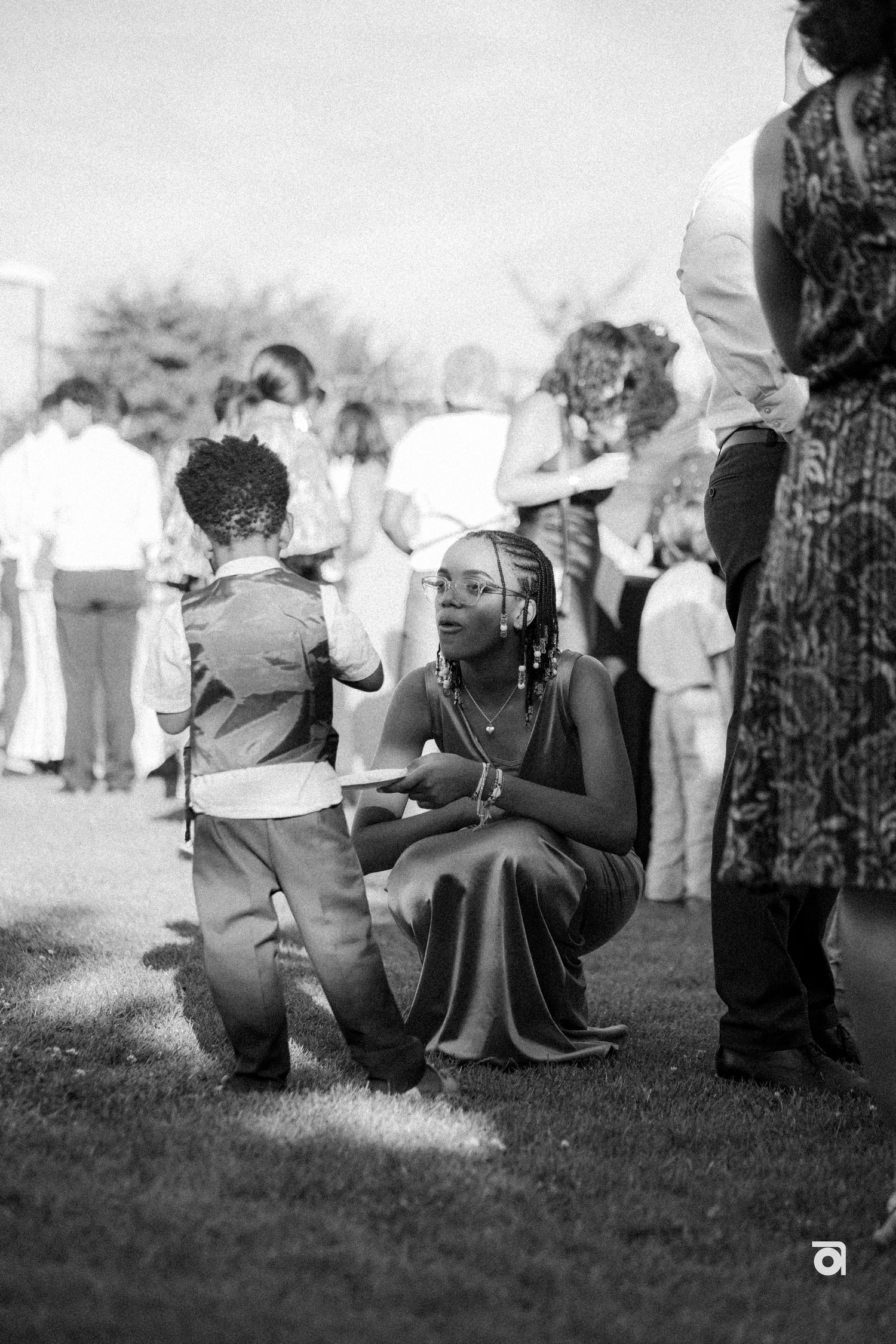 A candid black and white outdoor photo showing people interacting at a social gathering.