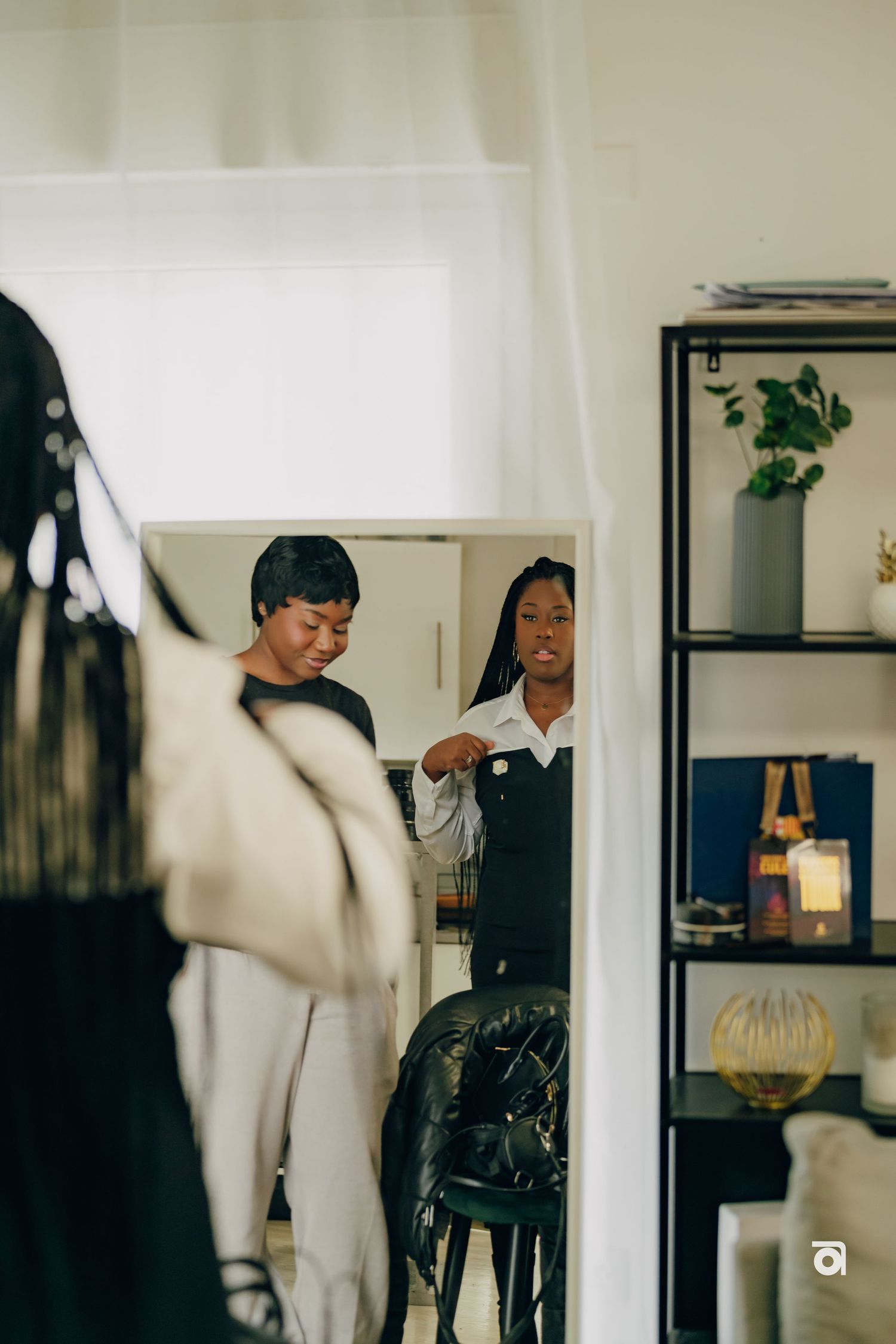 A mirror reflection capturing people getting ready in a room with shelving and decor.