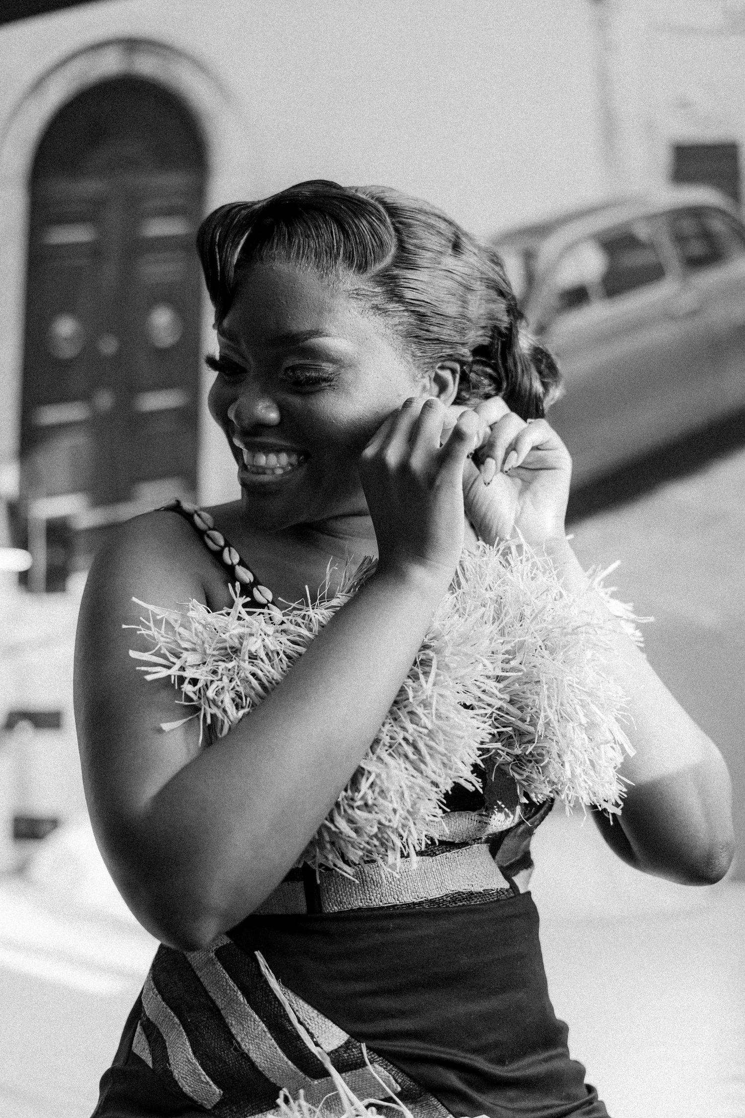 A joyful moment captured in black and white showing a radiant smile and feathered dress detail against an urban backdrop.