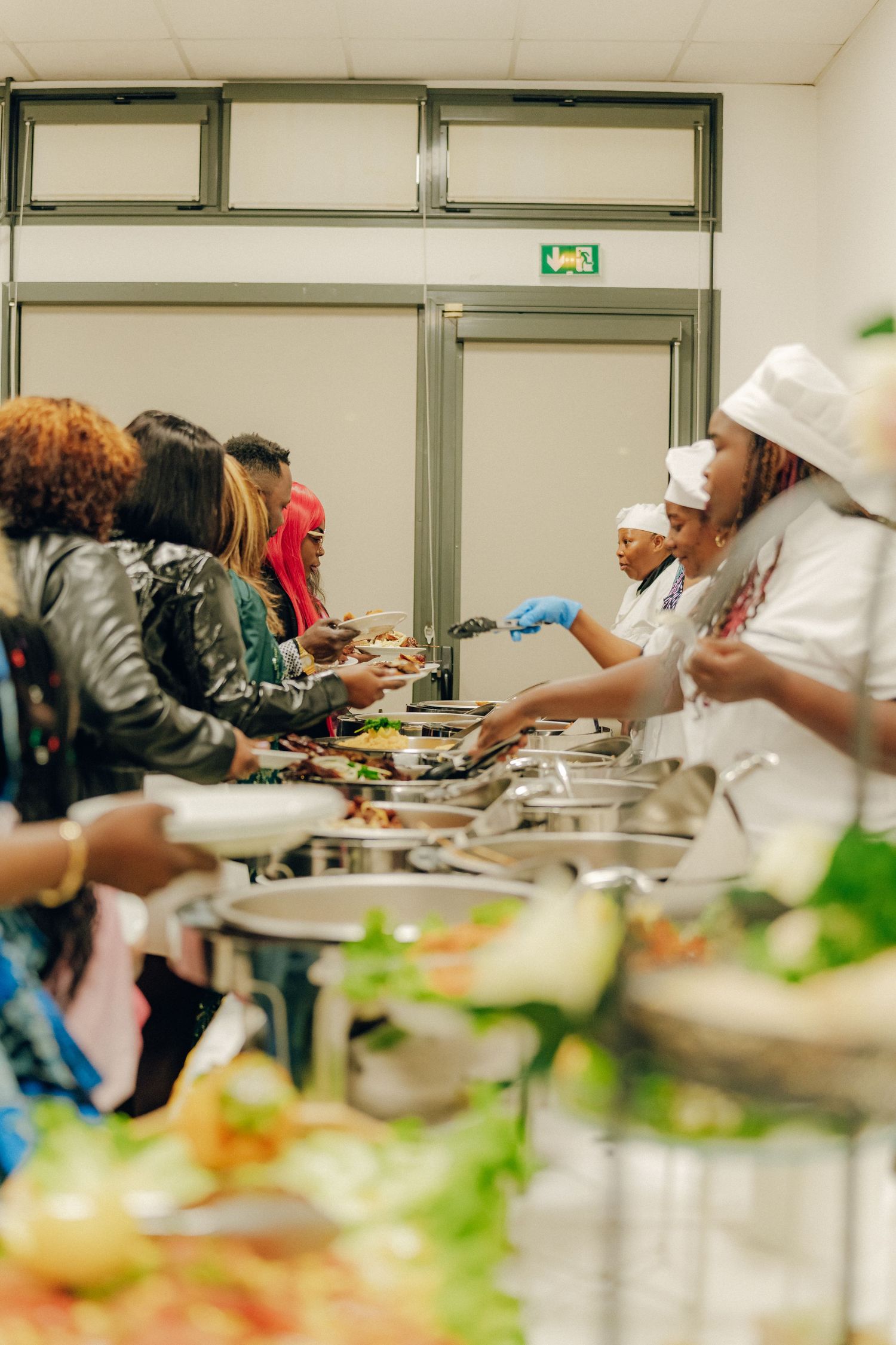 People serving themselves at a buffet line with chafing dishes and fresh salads.