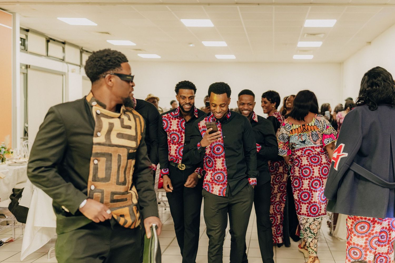 A group of attendees in formal and traditional attire gather in a hallway at a celebratory event.