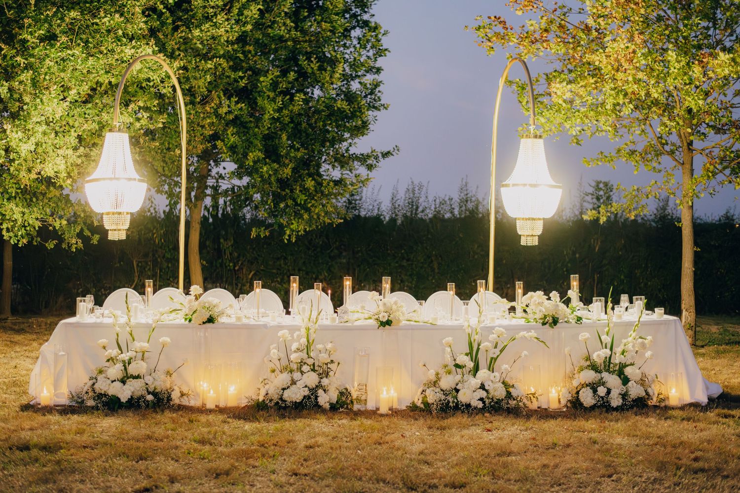 Outdoor wedding reception setup with white chairs and floral arrangements at sunset.