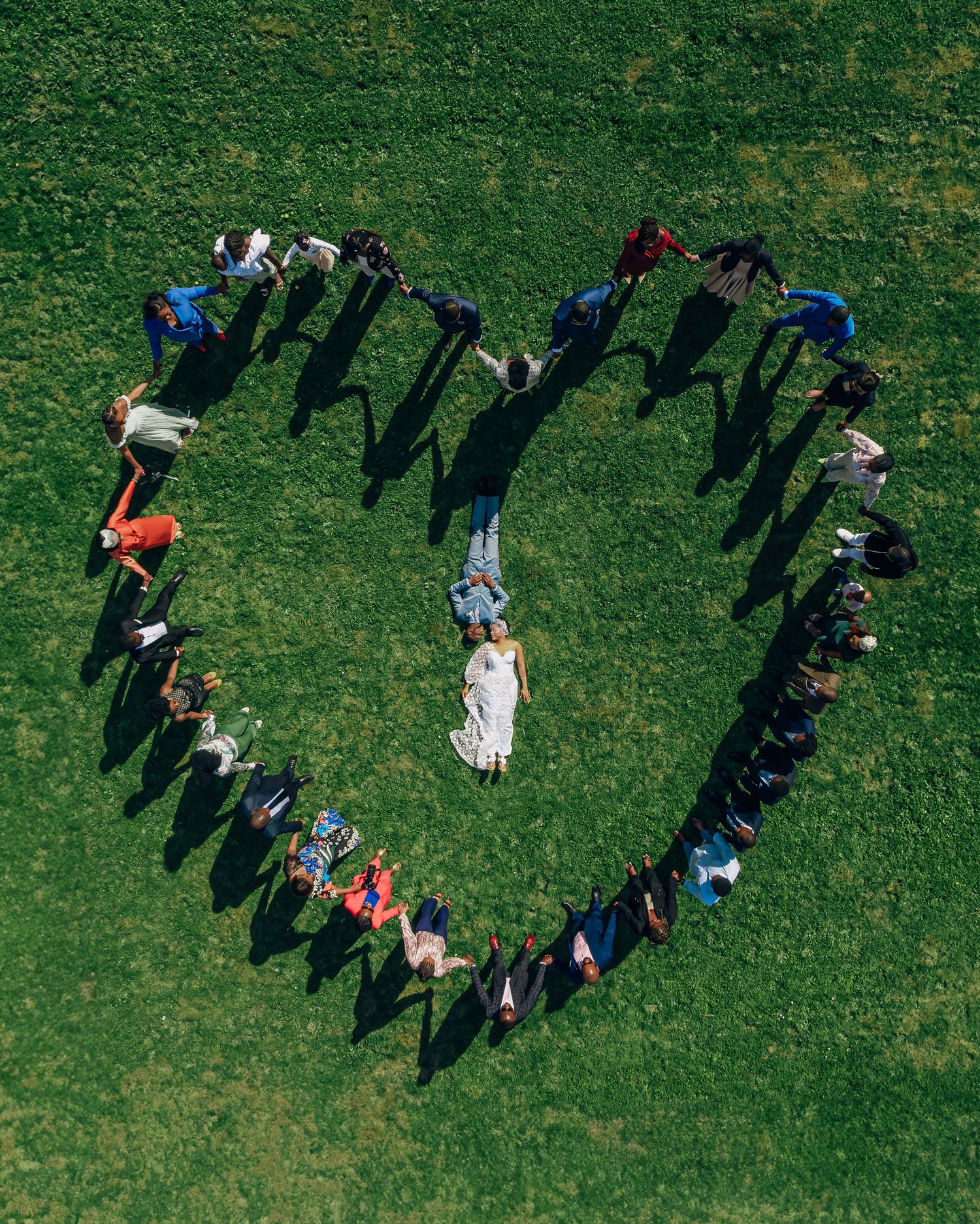 Aerial view of wedding party forming heart shape on green lawn.