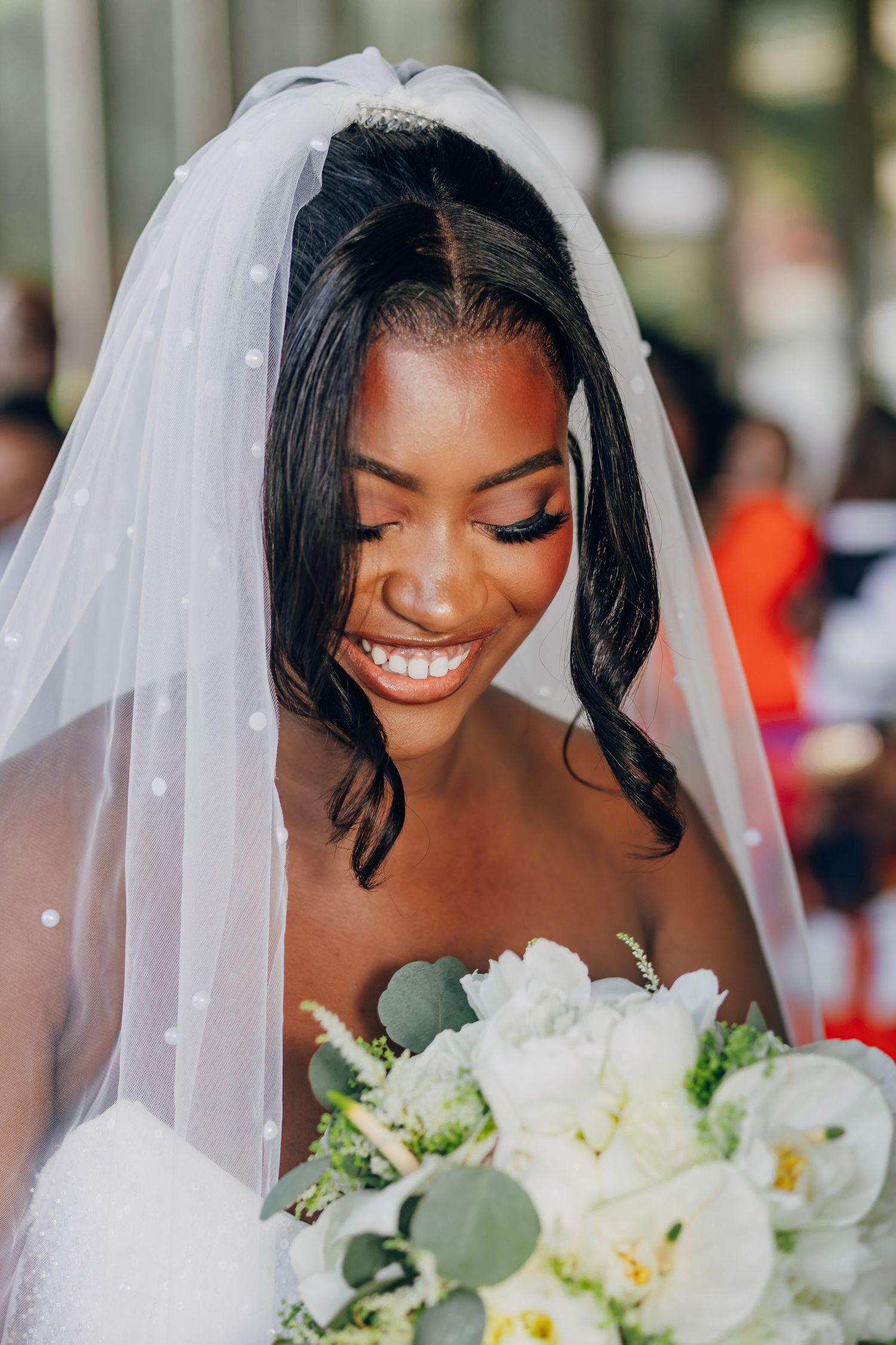 A radiant bride wearing a white veil holds a bouquet of white flowers and eucalyptus.