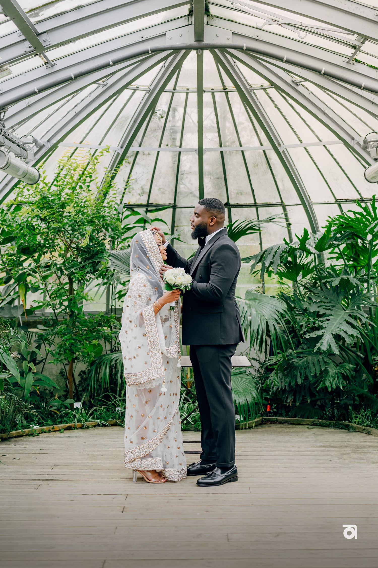 A romantic wedding photoshoot in a glass greenhouse conservatory surrounded by lush tropical plants.