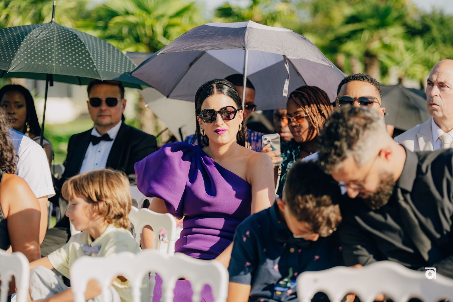 Wedding guests seated outdoors with umbrellas for shade during a summer ceremony.